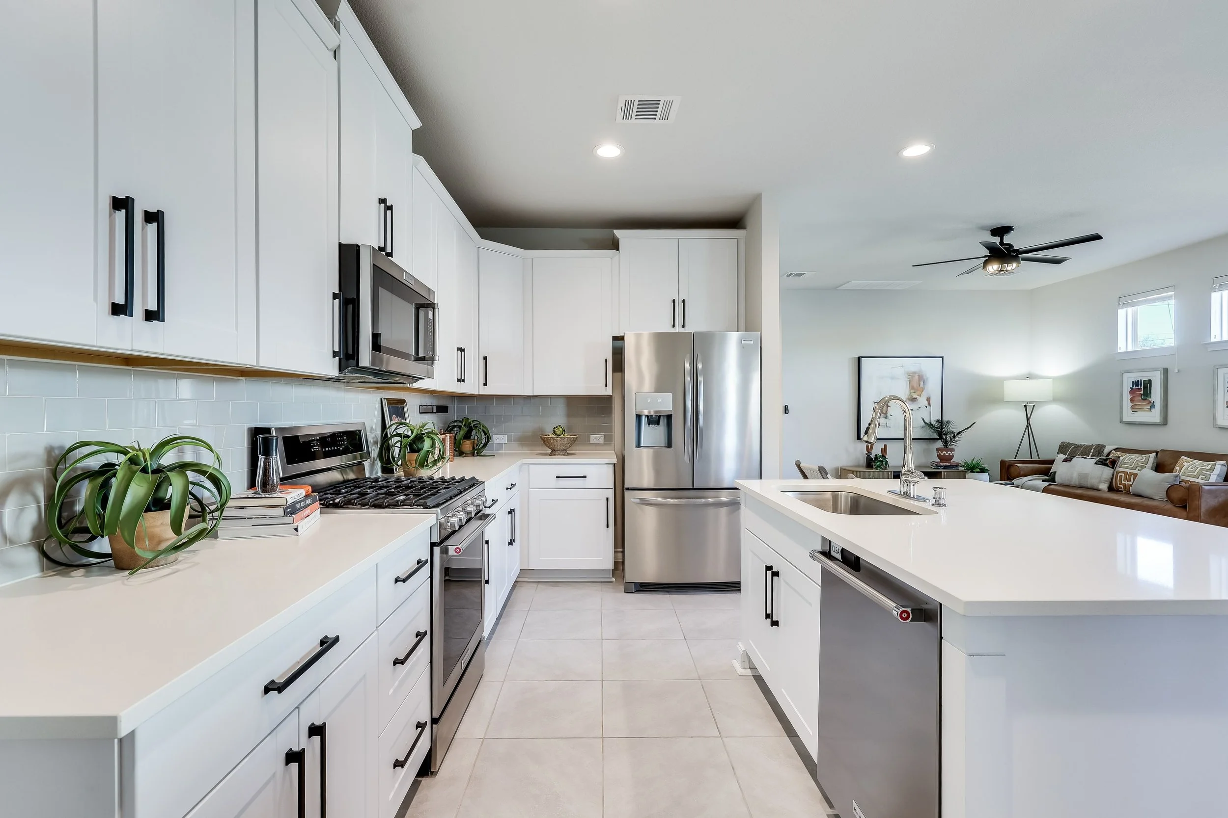 5216 Golden Canary Lane Austin, TX 78723. Modern kitchen with white cabinets, stainless steel appliances, and a white island with a sink, overlooking a living room with a couch, floor lamp, and artwork.