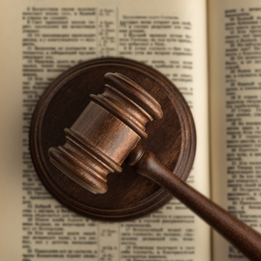 A judge's gavel resting on a circular base on top of an open law book with printed text.