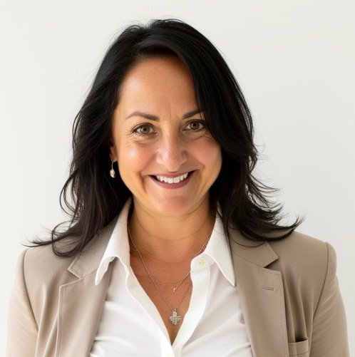 Indrani: A woman with shoulder-length dark hair, wearing a beige blazer, white shirt, and jewelry, standing against a white background.