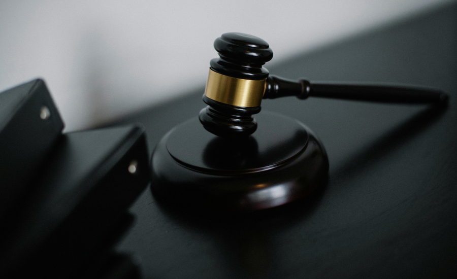 Close-up of a judge's gavel resting on a sound block on a dark surface, with a blurred background.
