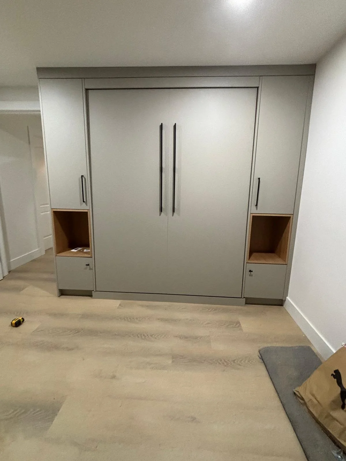 Gray built-in cabinet with two tall handles in middle, and smaller areas with open shelves and drawers on each side, in a room with light wood flooring.