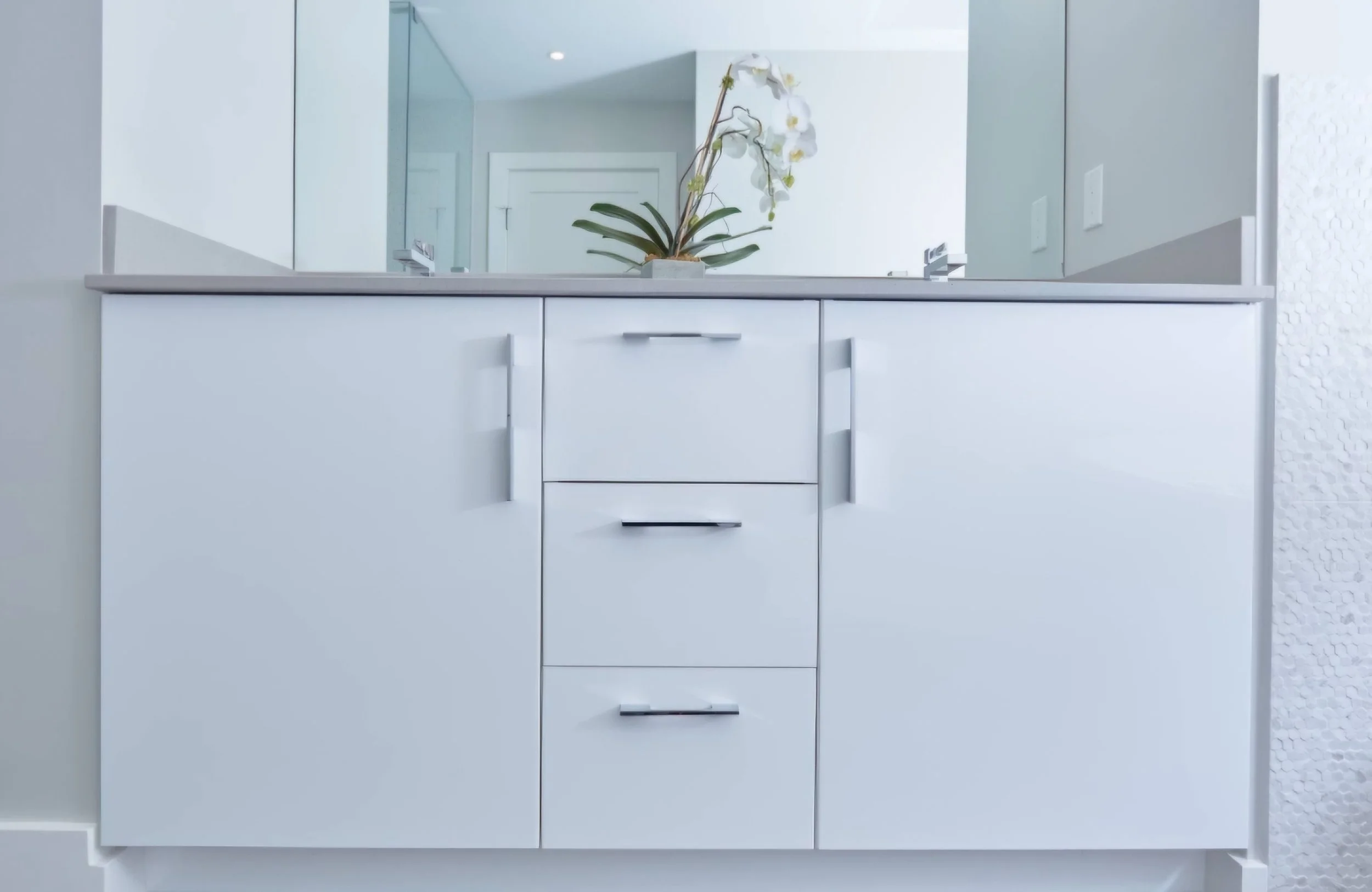 White bathroom vanity with a potted orchid on top, a mirror above, and a textured wall to the right.