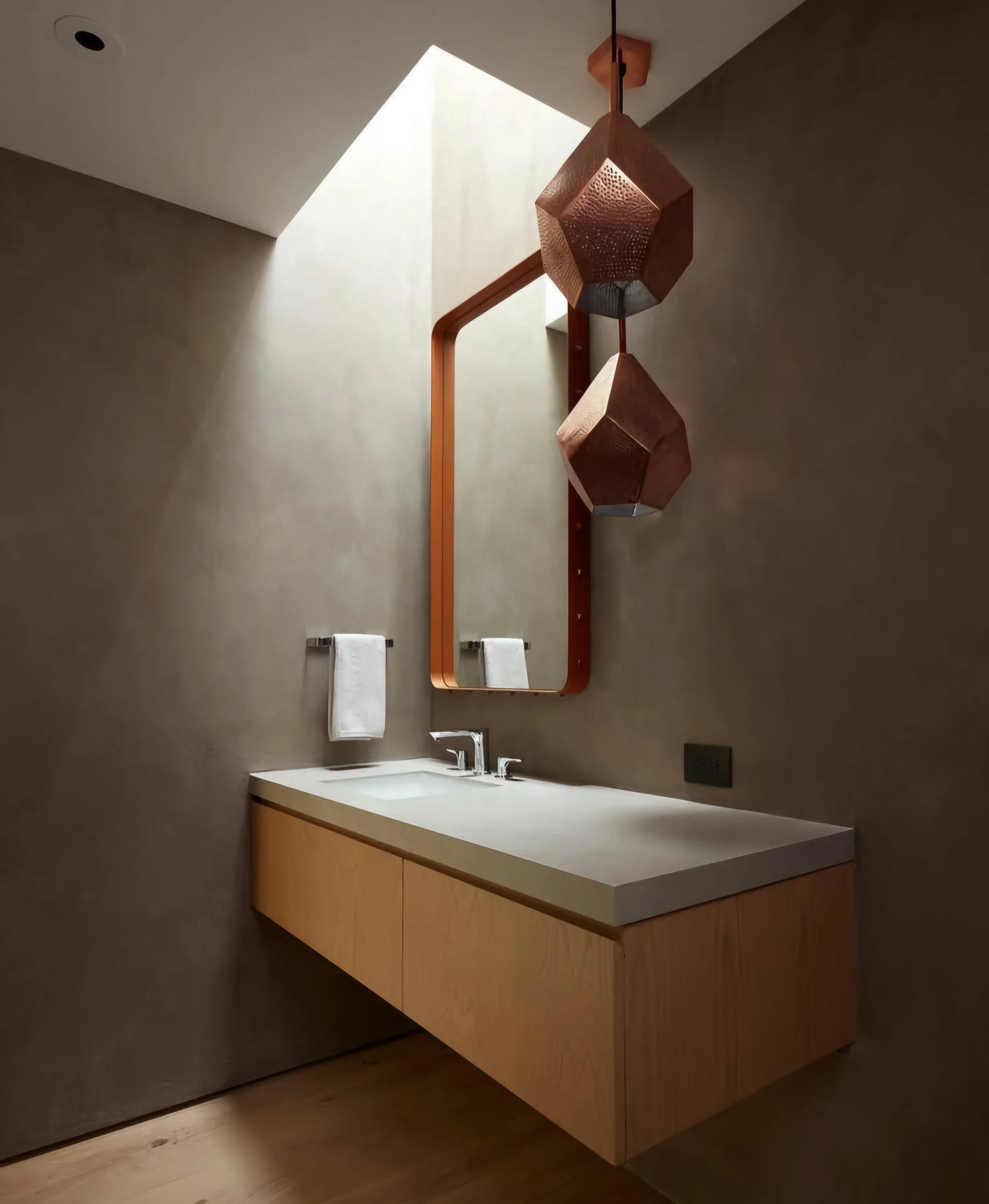 Modern bathroom with a floating wooden vanity, white countertop, twin sinks, a large rectangular mirror with a copper frame, and two copper pendant lights hanging from the ceiling.