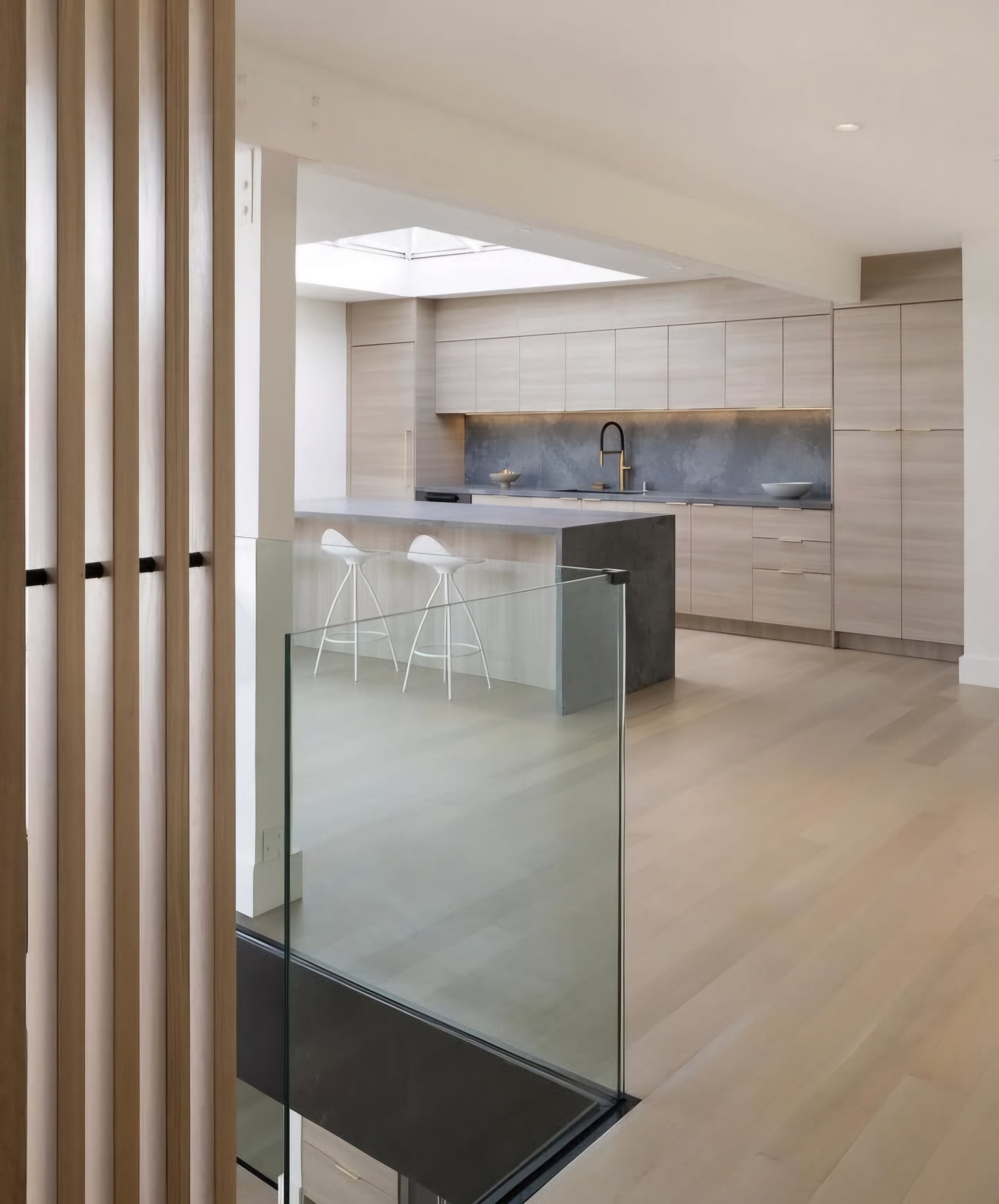 Modern kitchen with light wood cabinetry, a skylight, and a kitchen island with two white barstools.