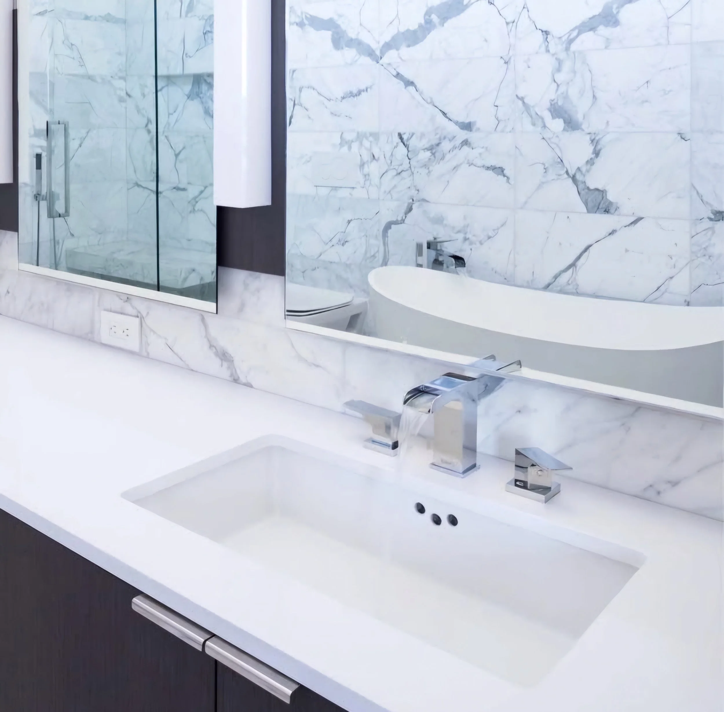 Modern bathroom with white marble countertop and wall, featuring an integrated sink, chrome faucet, and a large mirror reflecting a bathtub with a marble wall backdrop.