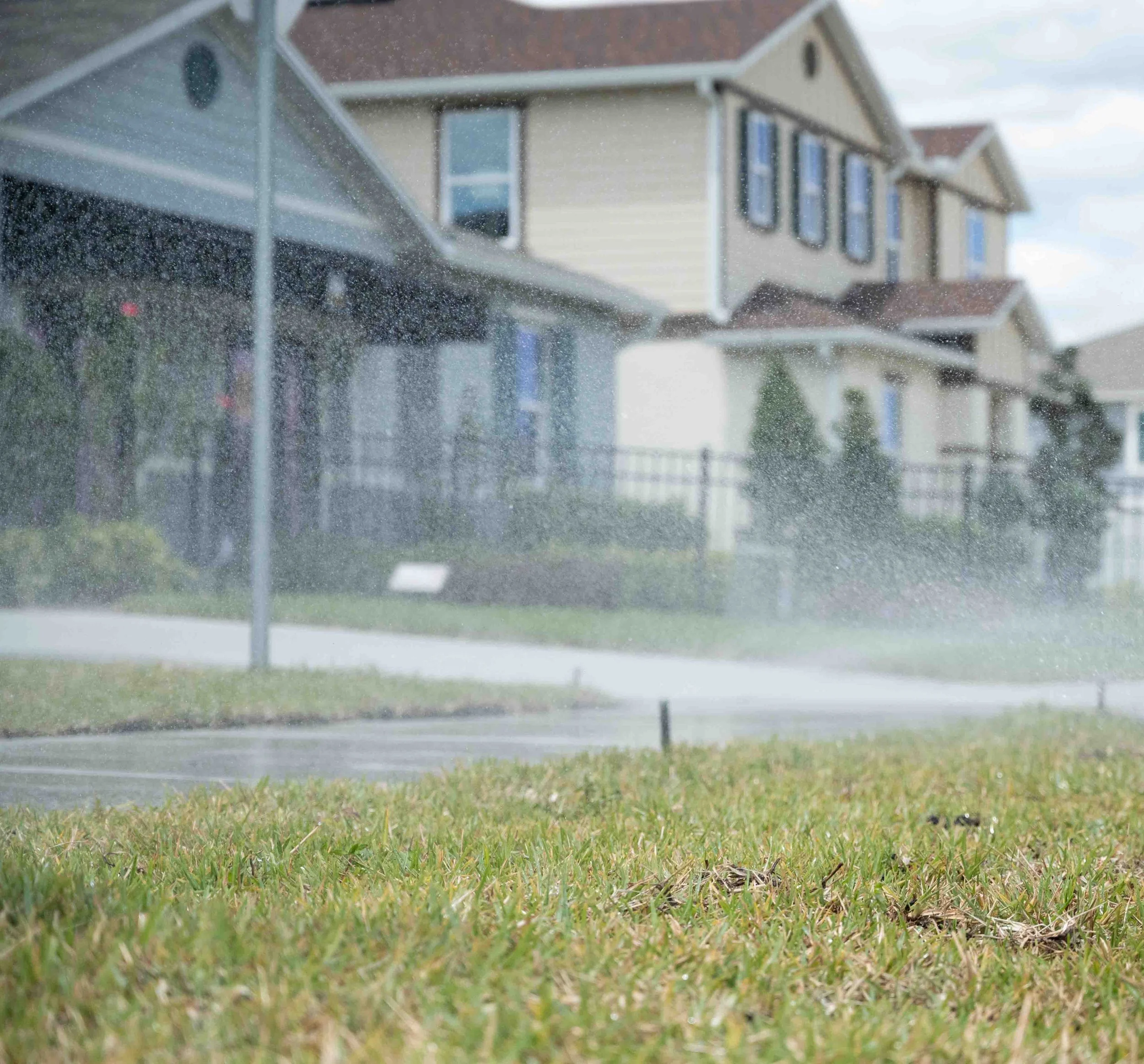 View of residential houses through a rain-spattered window, with a wet residential lawn installed by a local sod farm.