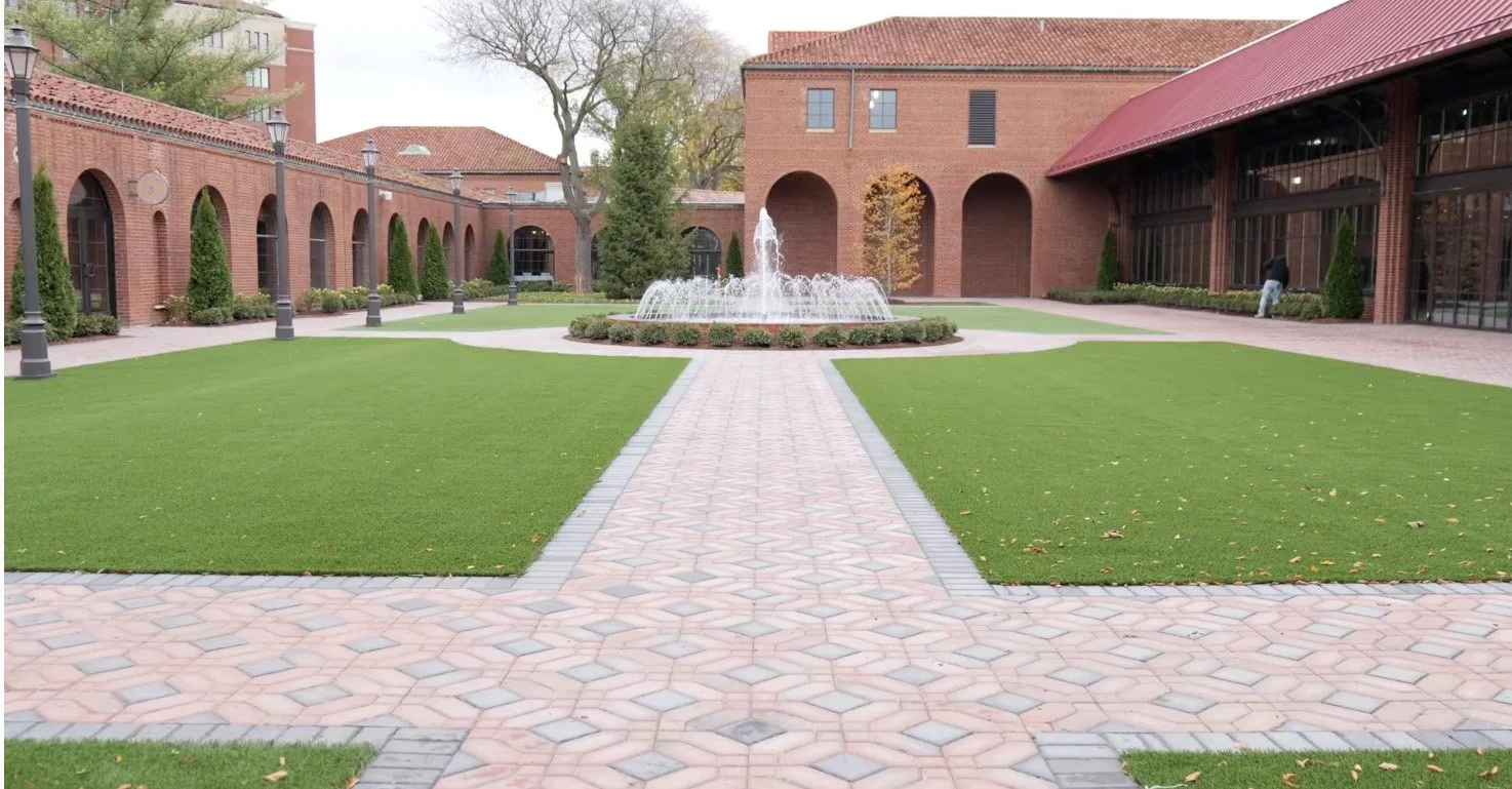 A courtyard with a brick building on each side, a central fountain, and green commercial sod surrounding the properties' greenspace.