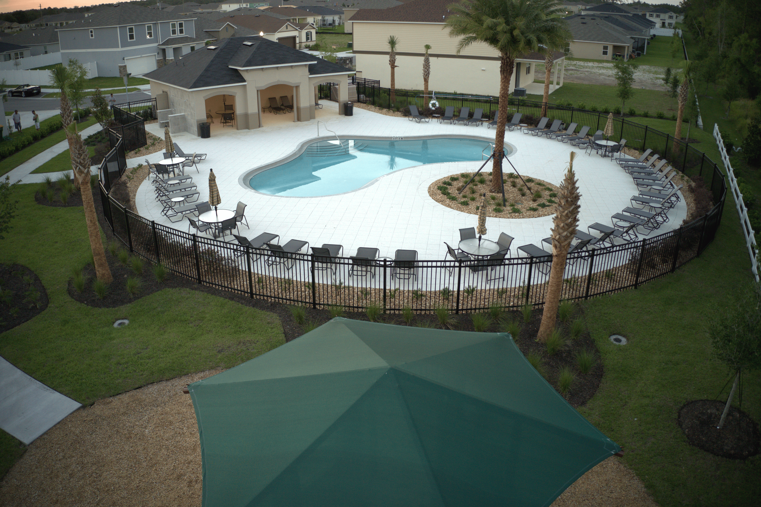An outdoor swimming pool area in a residential community with lounge chairs, tables with umbrellas, surrounded by direct from farm kentucky bluegrass sod.