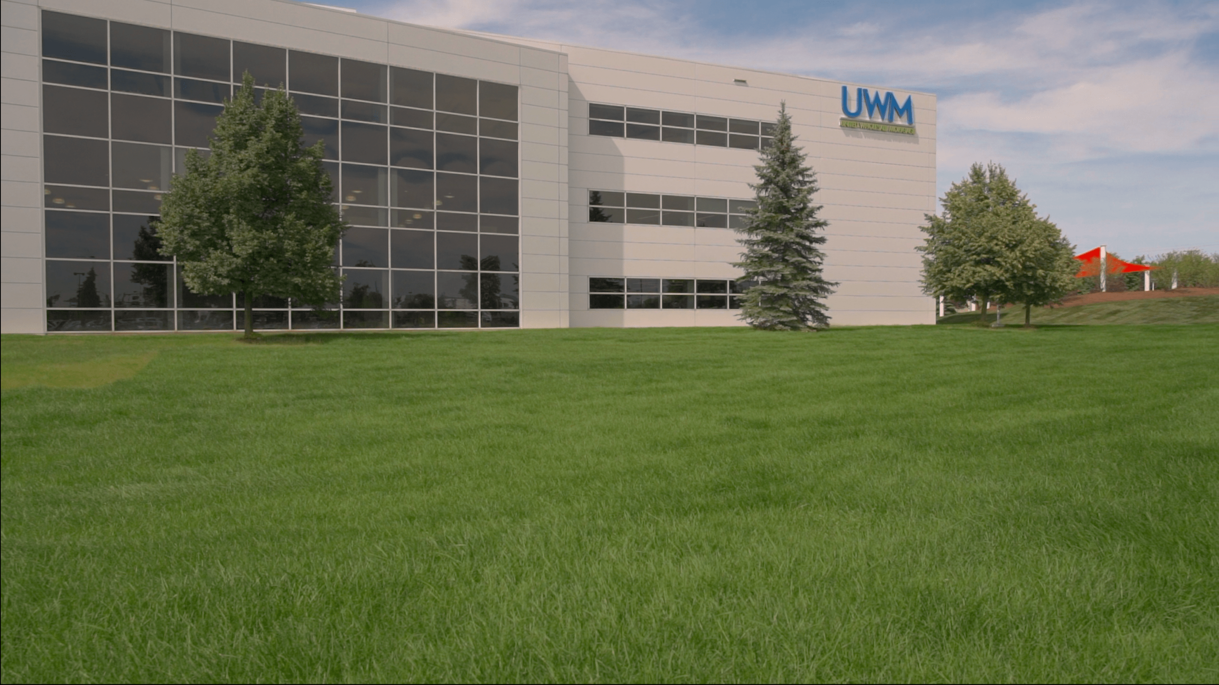 Modern white commercial building with large glass windows and the blue UWM sign, surrounded by fresh kentucky bluegrass and trees under a partly cloudy sky.