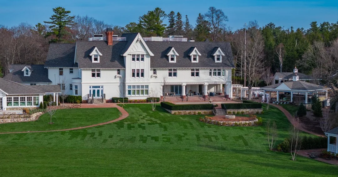 Large white house with multiple pitched roofs and dormer windows, surrounded by a well-maintained lawn provided and installed by Meadowbrook Acres.
