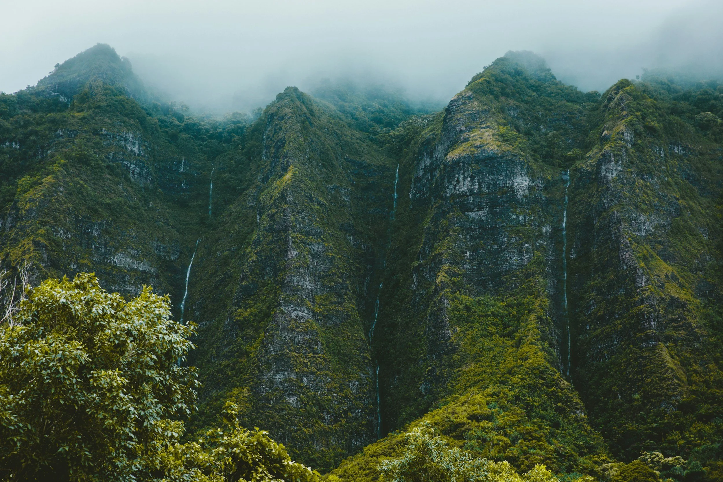 Lush green mountains with waterfalls and mist covering the peaks.