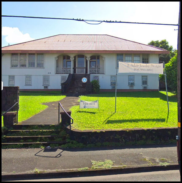A two-story white building with a red-tiled roof, front stairs, and a sign for Adair Jewelry Design on a grassy lawn with a sidewalk and steps.