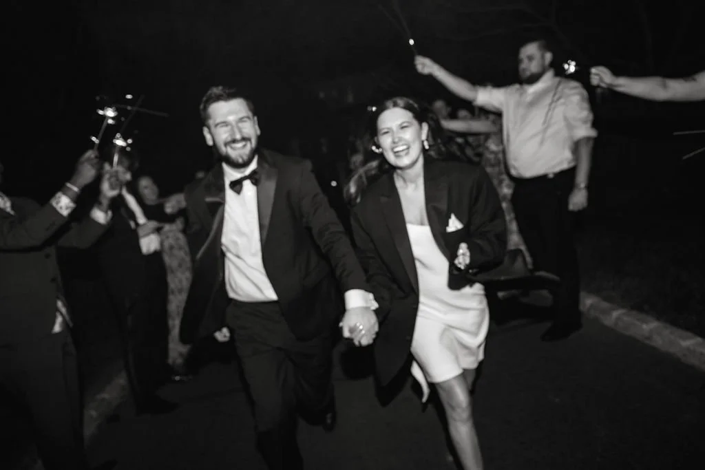 A group of people celebrating at night, with a couple holding hands and smiling, surrounded by others holding sparklers.