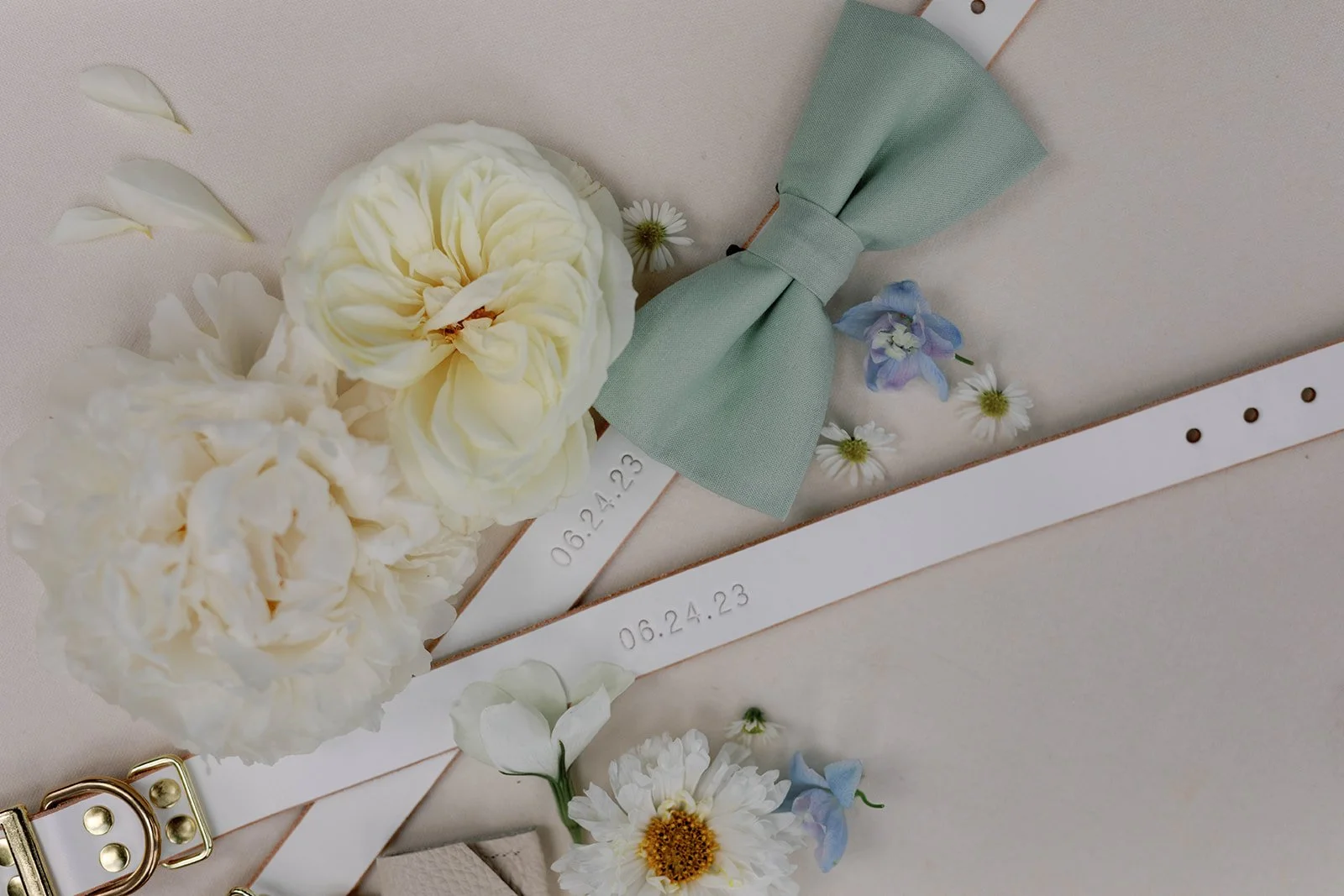 Cream-colored flowers, a light green bow, white ribbons with embossed dates '08.24.23' and '06.24.23', and small assorted flowers on a light background.