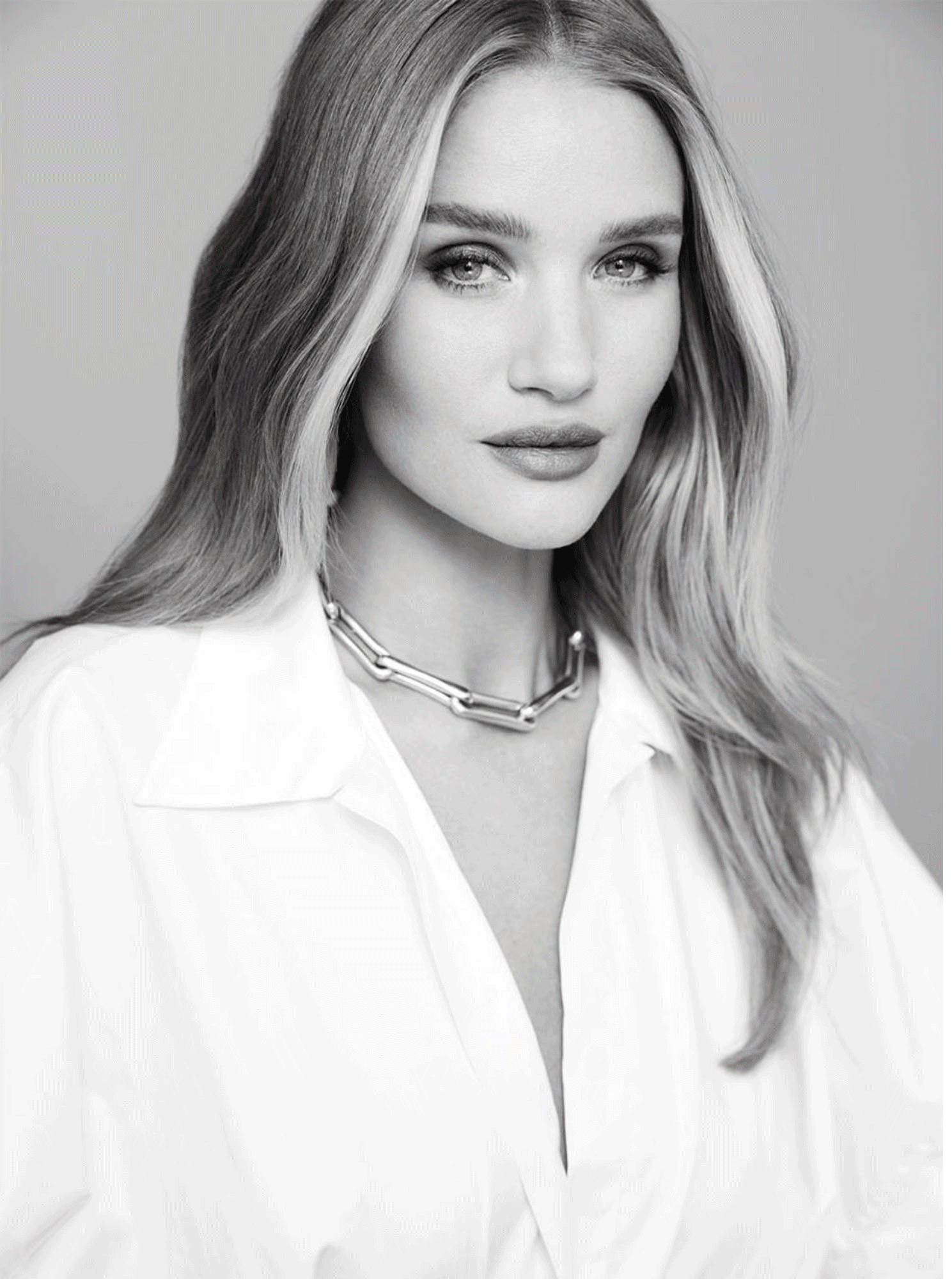 Black and white portrait of a woman with long wavy hair, wearing a collared shirt and a chunky chain necklace.