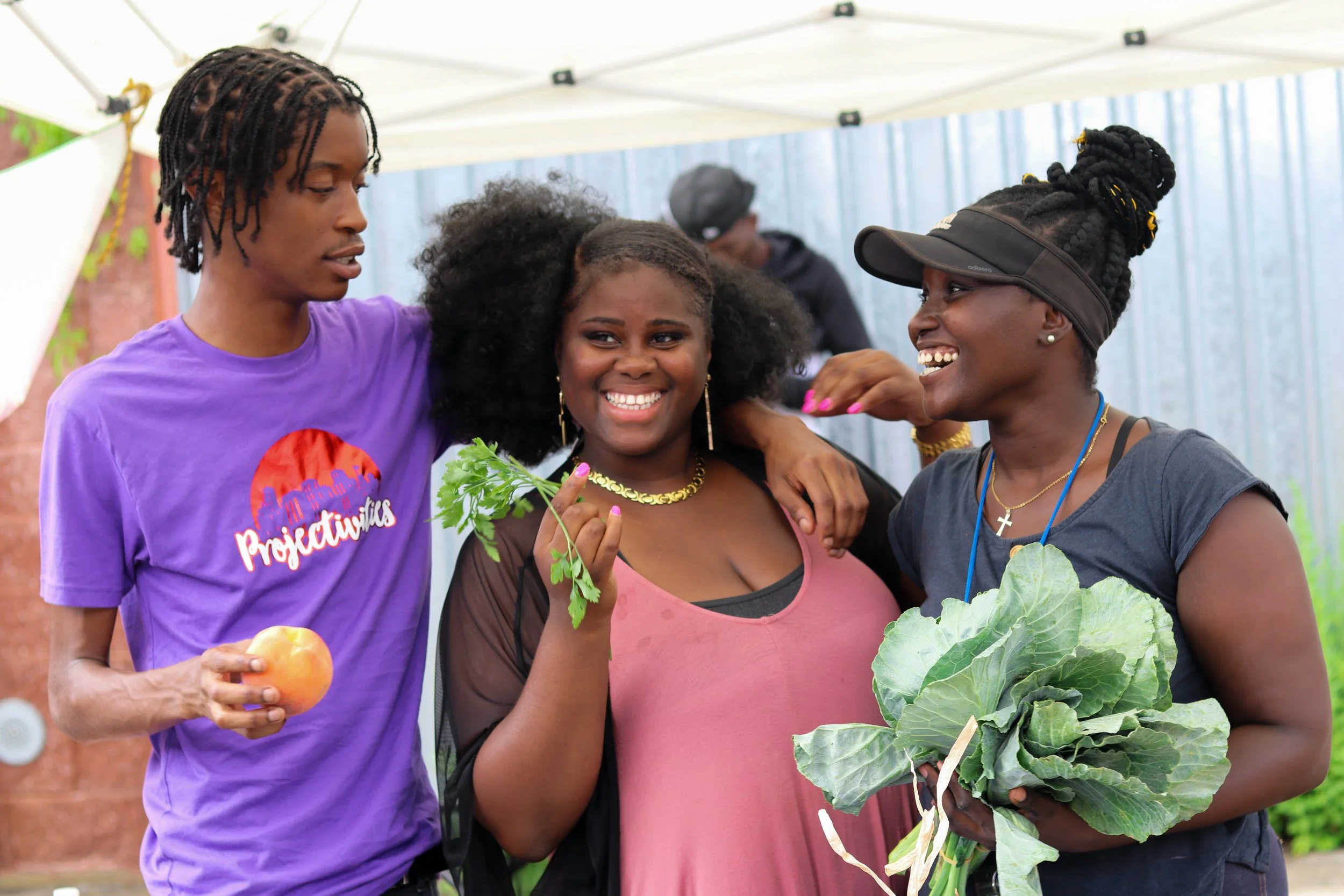 3 people smiling and holding freshly grown crops