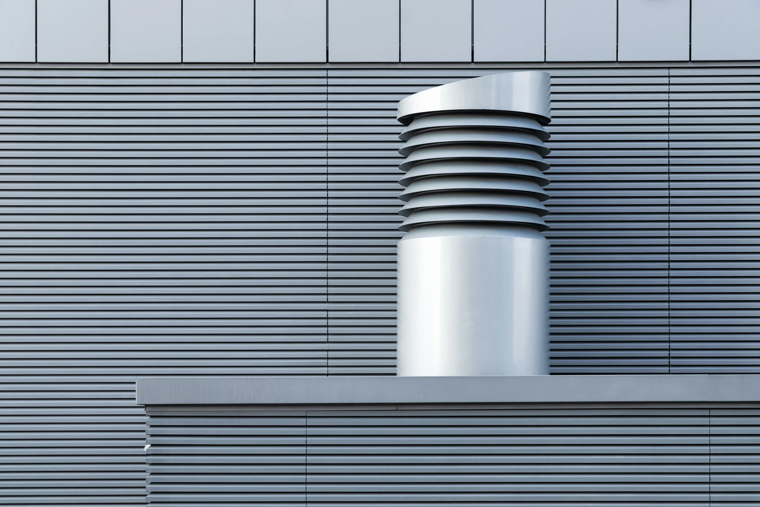 Modern building exterior with horizontal metal siding and a metallic vent with angled louvers.