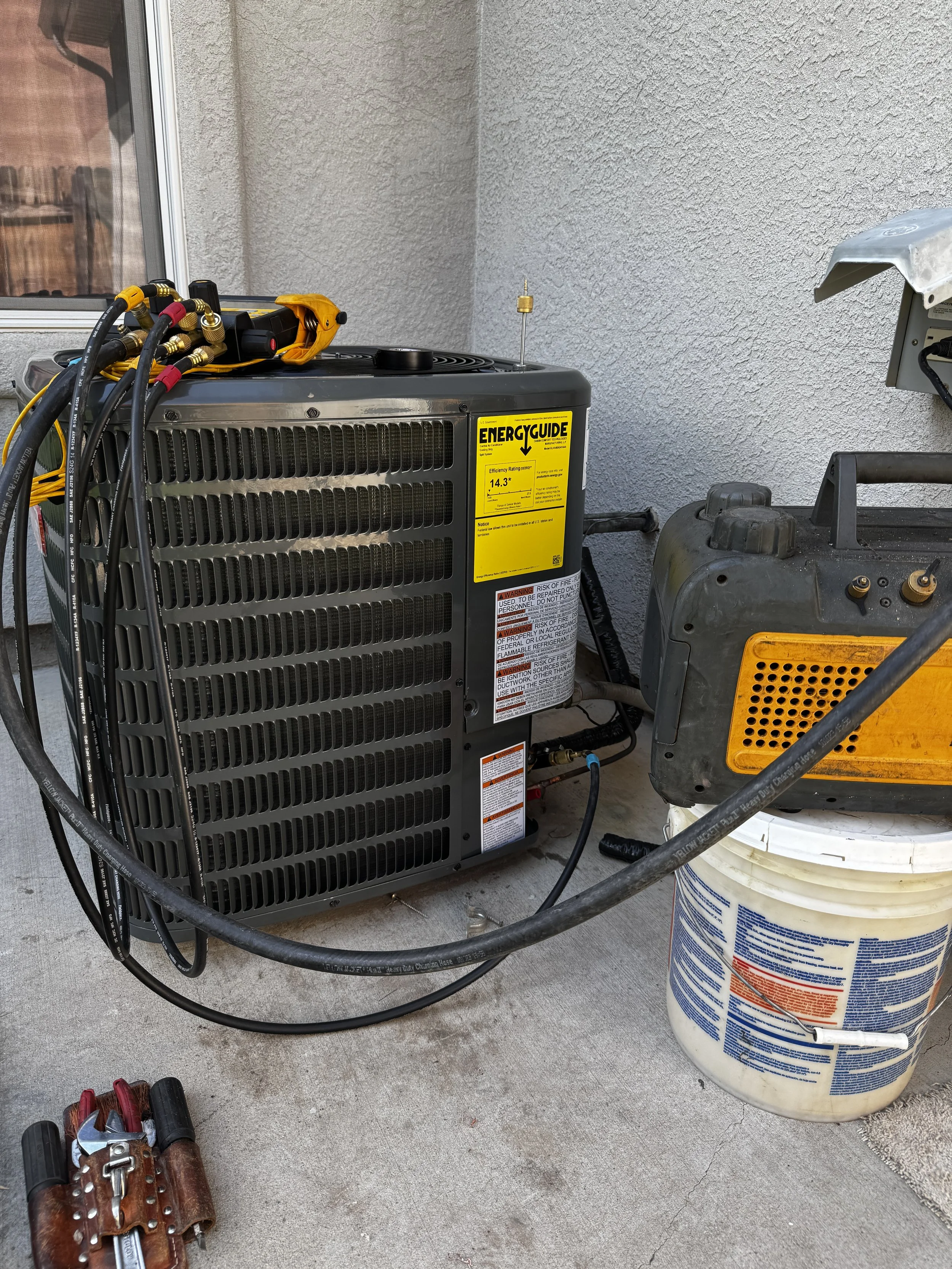 HVAC unit with tools and equipment nearby on a concrete patio outside a house.