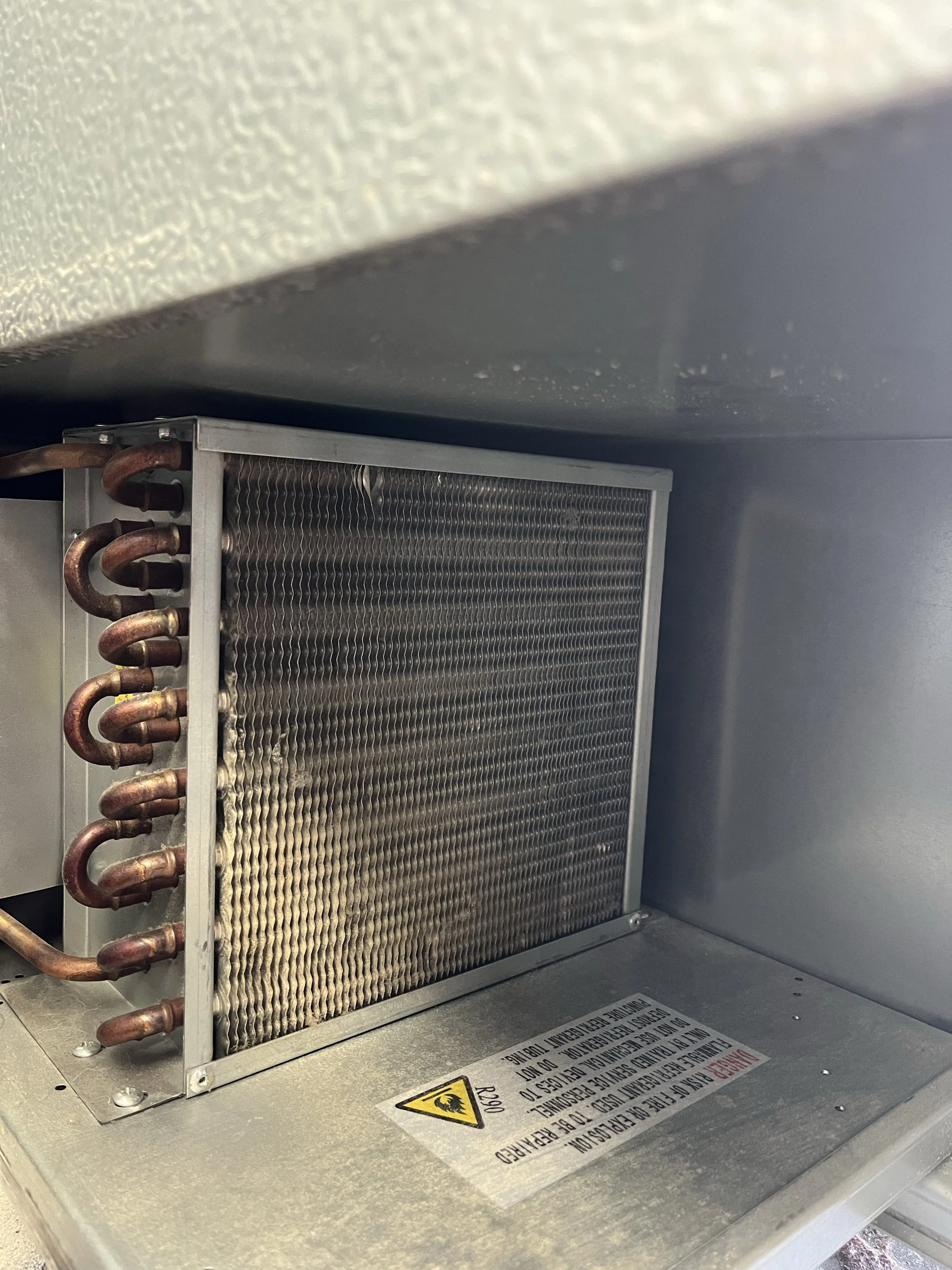 Close-up of an electronic or refrigeration unit with copper tubing and a warning label