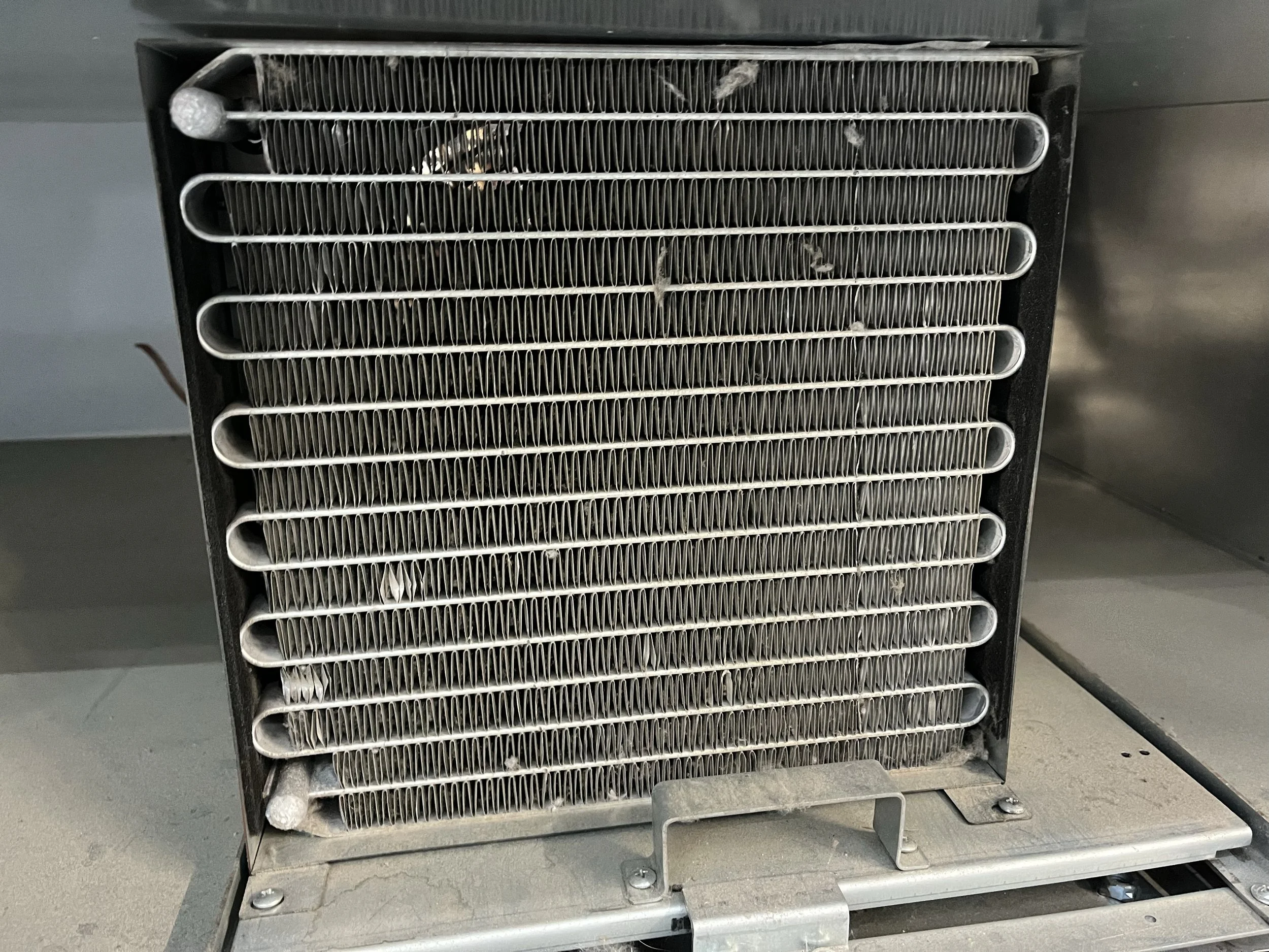 Close-up of an air conditioning or refrigeration unit's heat exchanger/evaporator coil with dust and debris.
