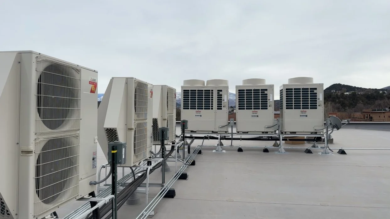 Multiple air conditioning units on a rooftop with mountains in the background.