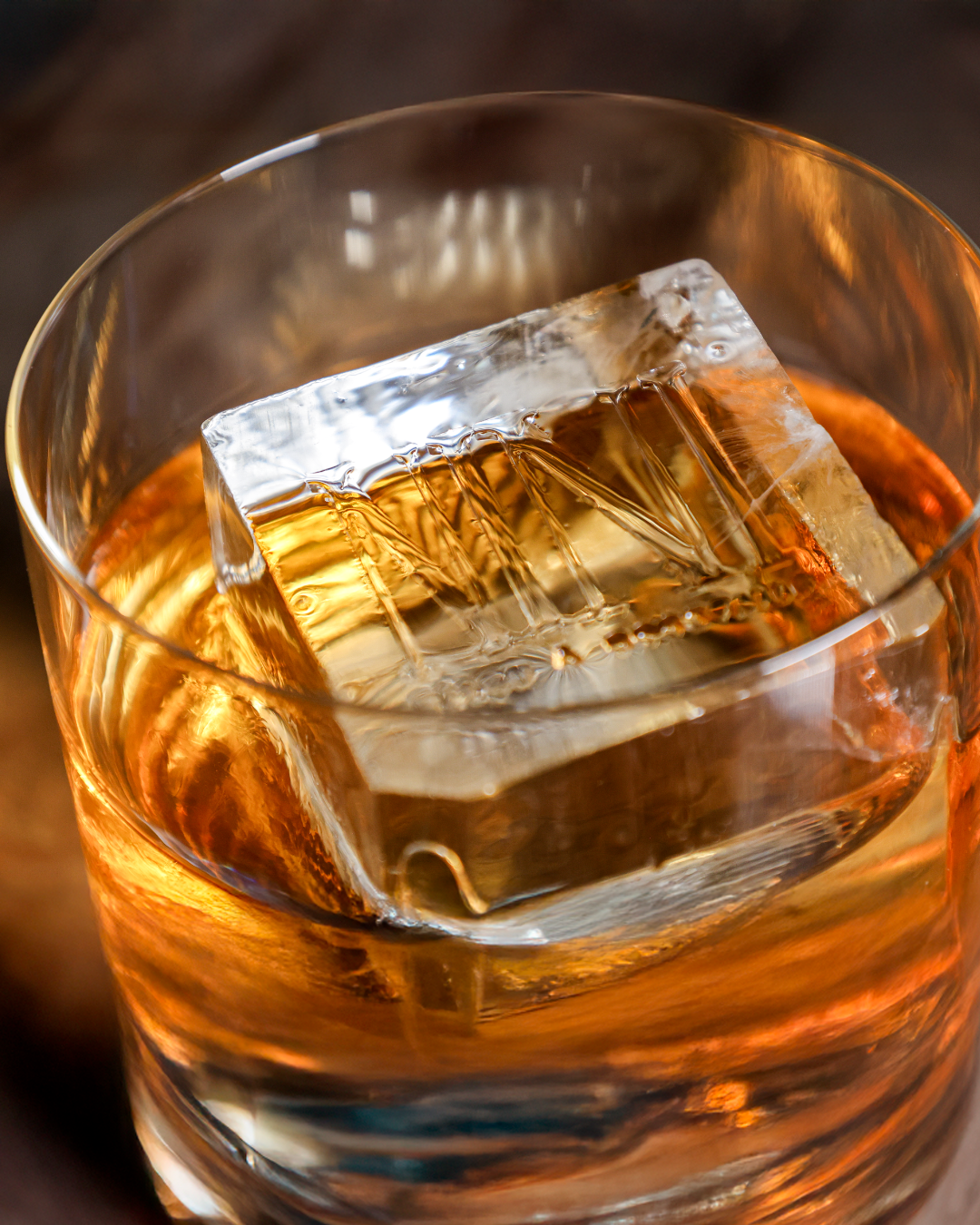 Close-up of a glass of whiskey with a large ice cube.