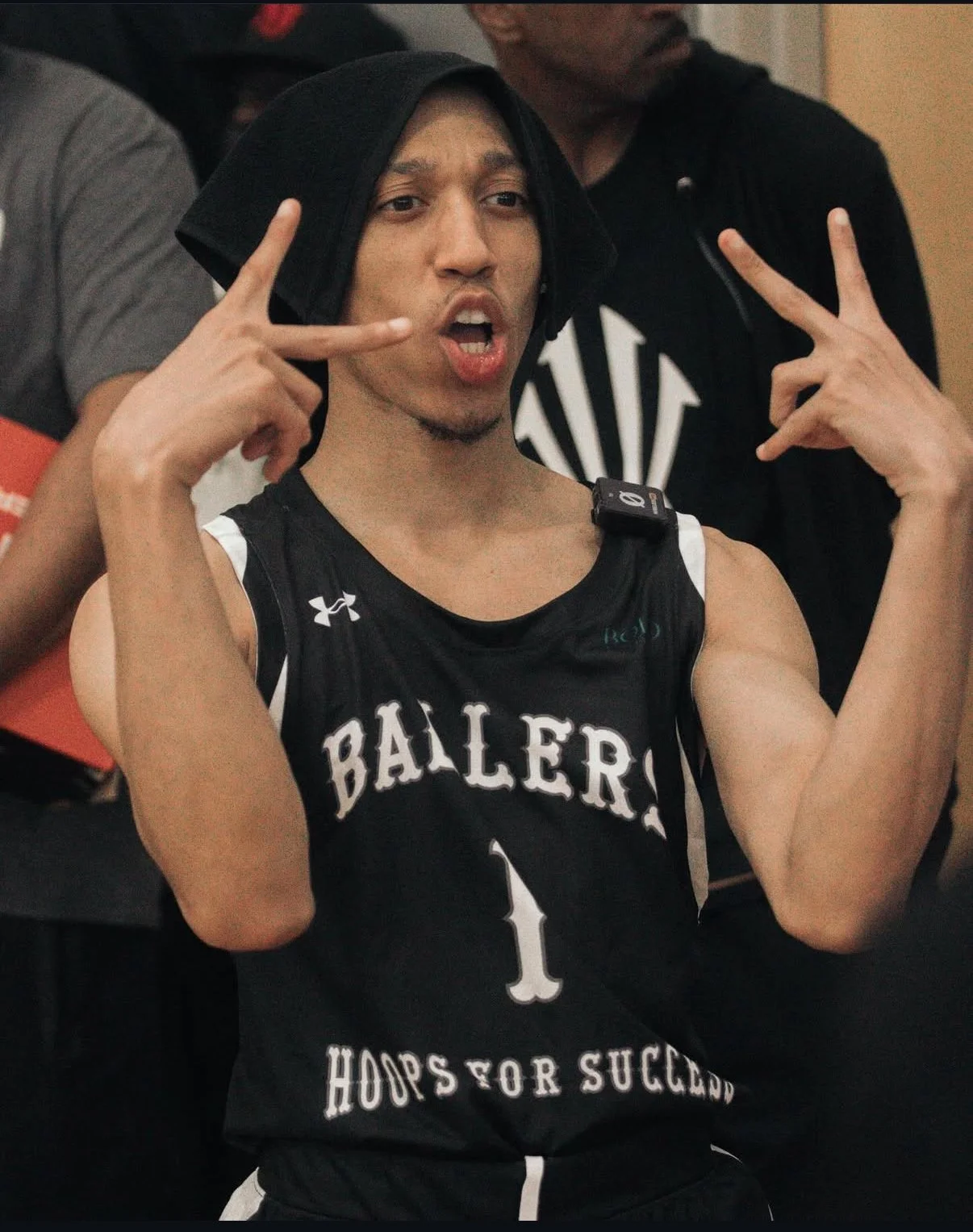Young man in a basketball jersey making peace signs near his face at a sports event.