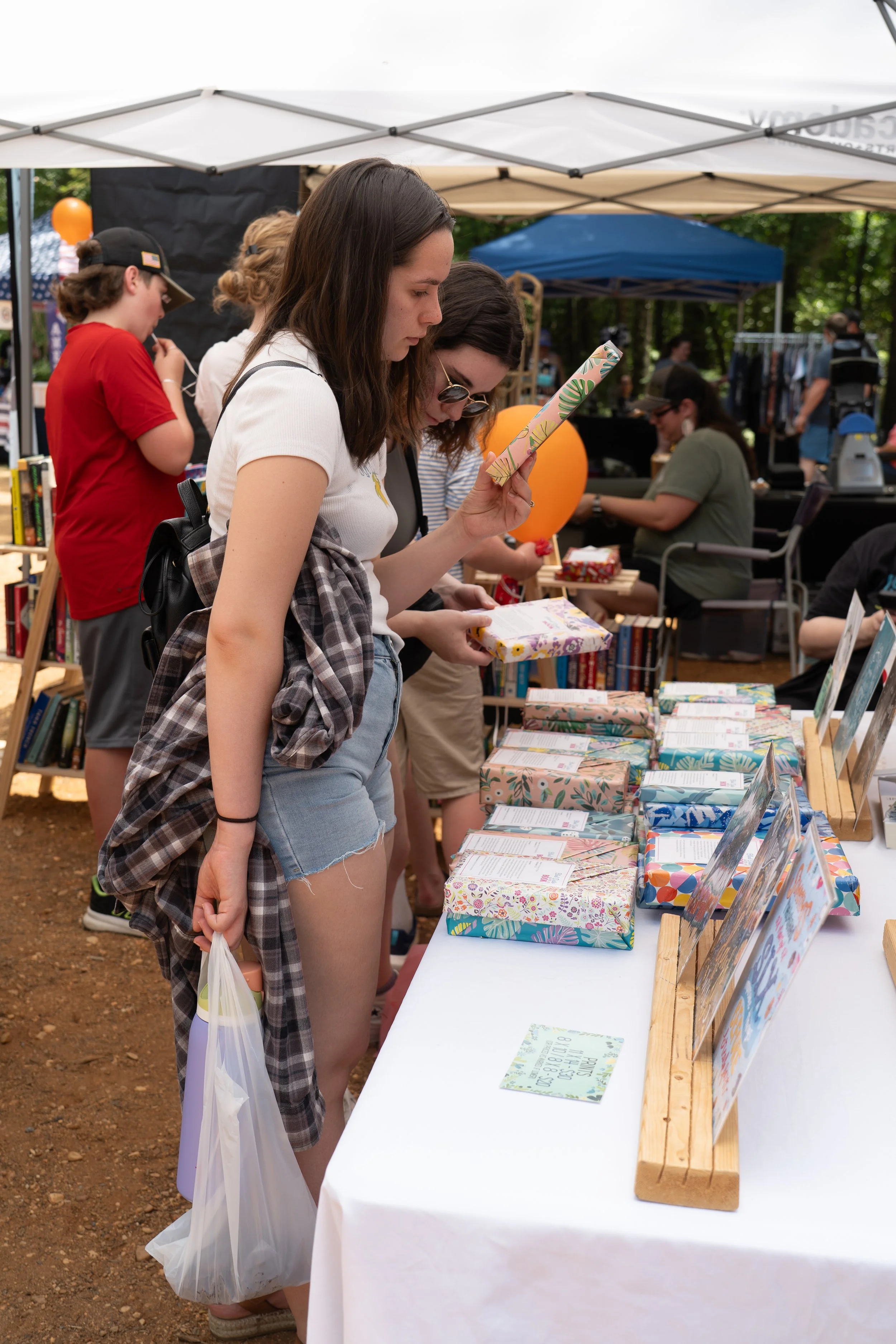 People shopping for books at an outdoor market stall with wrapped books and informational signs.