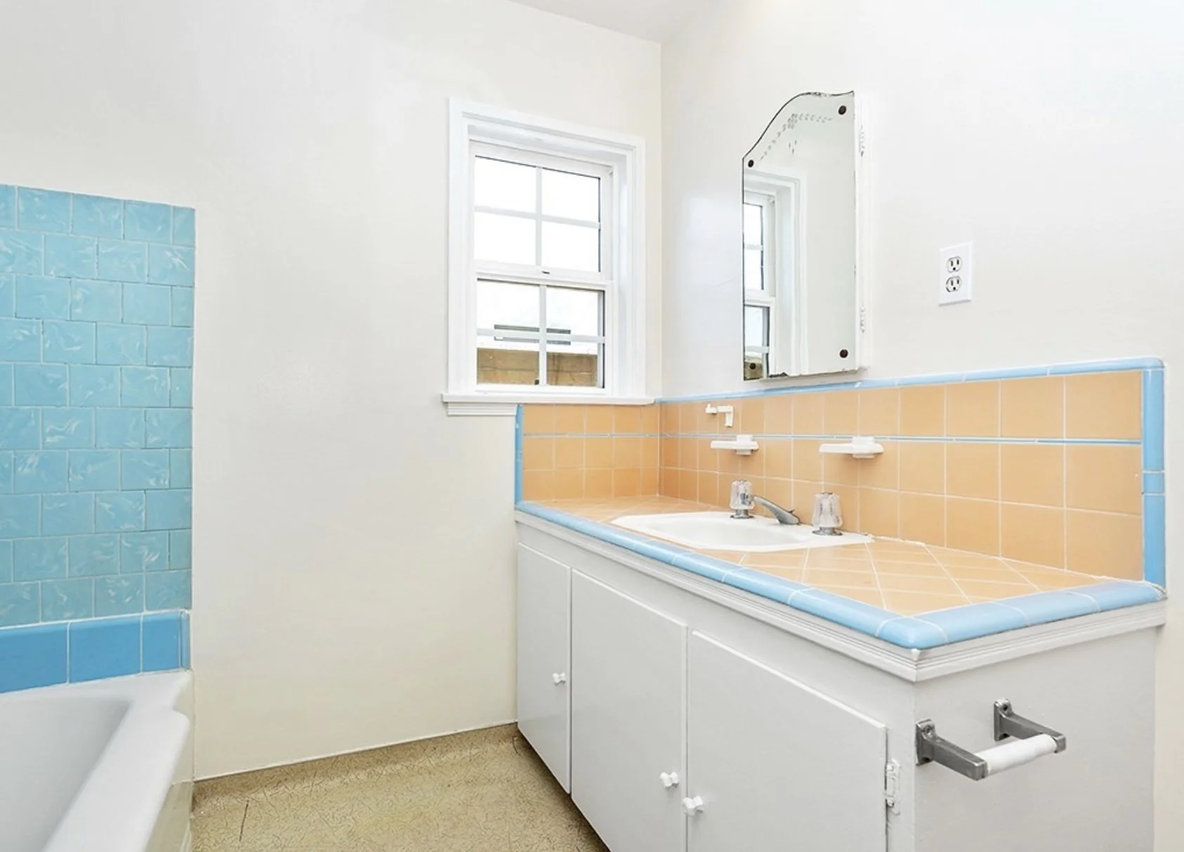 Bathroom with a white cabinet vanity, peach and blue tiled countertop, a mirror, a window, and a partial view of a blue-tiled shower on the left at residence 5645 & 5645 ½ Auckland Ave, in North Hollywood, California.