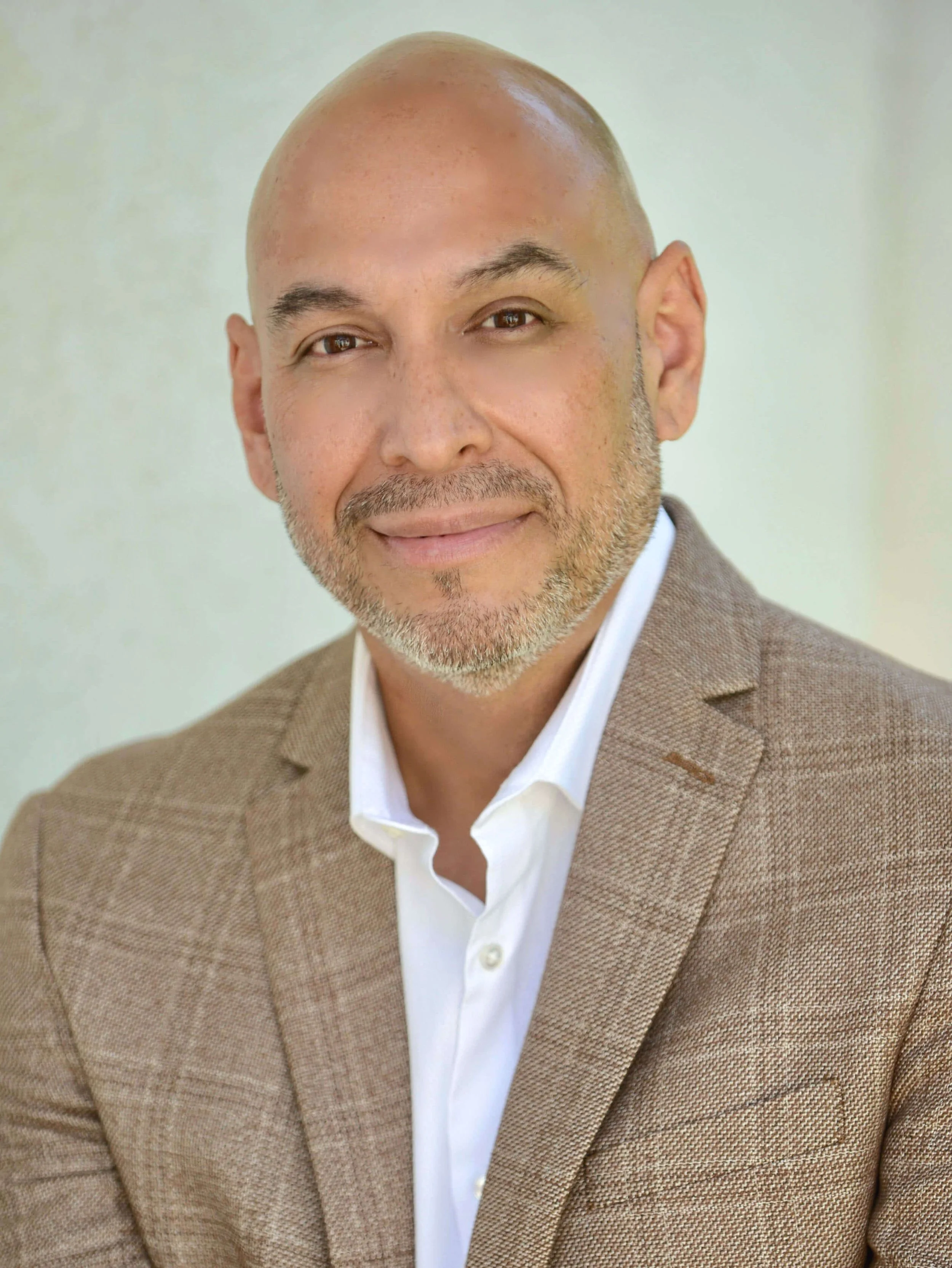 John Canto: founder of BELLEVRA Group shown in a brown plaid suit against a grey background.