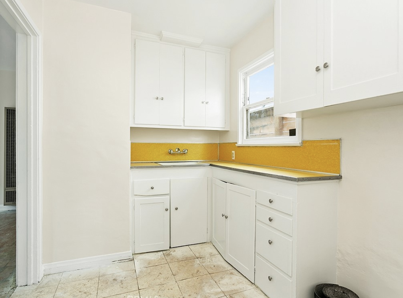 Empty kitchen with white cabinets, yellow backsplash, a window, and a tiled floor at residence 5645 & 5645 ½ Auckland Ave, in North Hollywood, California