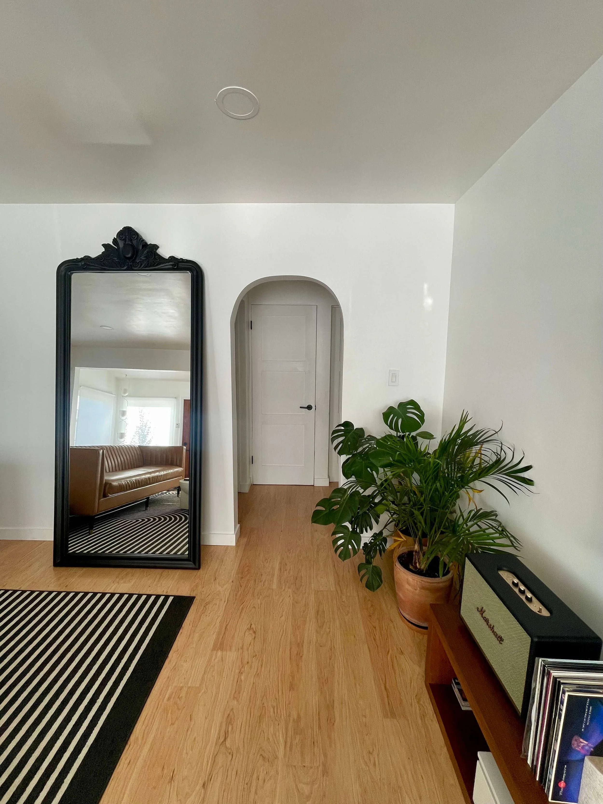 Interior of a newly renovated living room at 6605 & 6603 4th Ave in Hyde Park featuring an archway, plants, oversized mirror and a linear pattern black and white rug.
