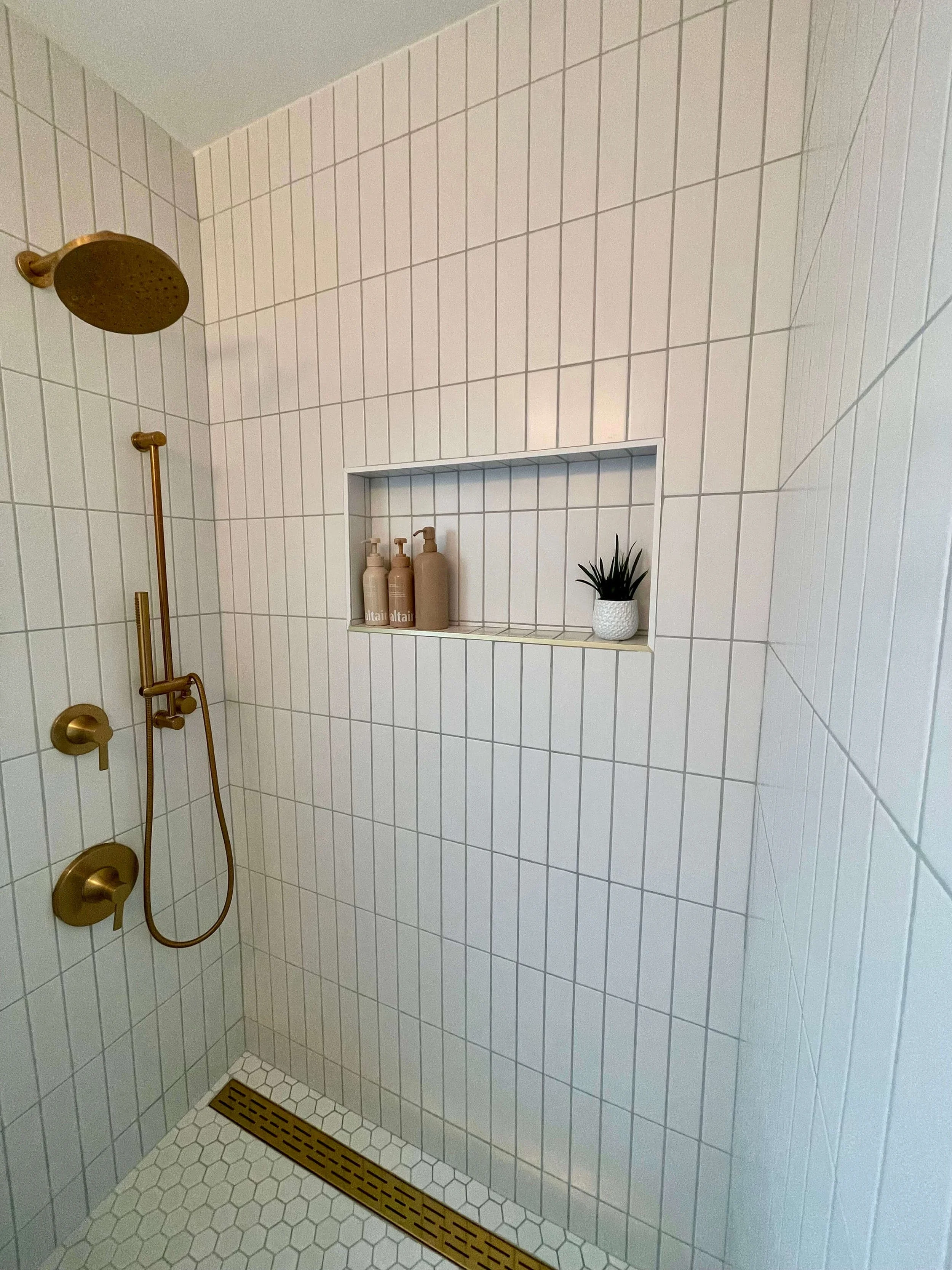 Newly renovated white tile shower at 6605 & 6603 4th Ave in Hyde Park featuring brass gold fixture accents.