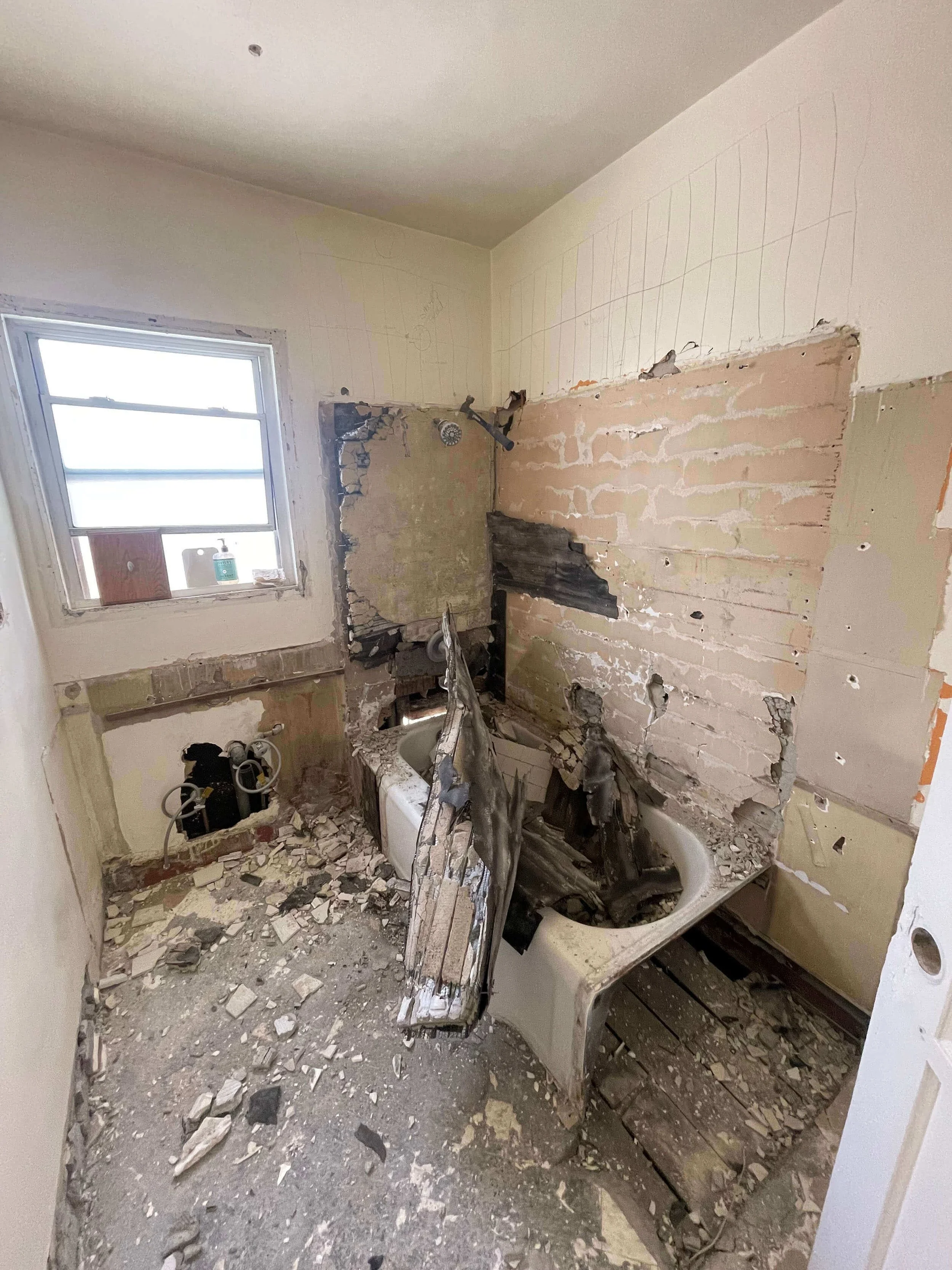 A bathroom in disrepair, with a bathtub, collapsed wall, exposed pipes, and debris on the floor at residence 6605 & 6603 4th Ave. before renovation.