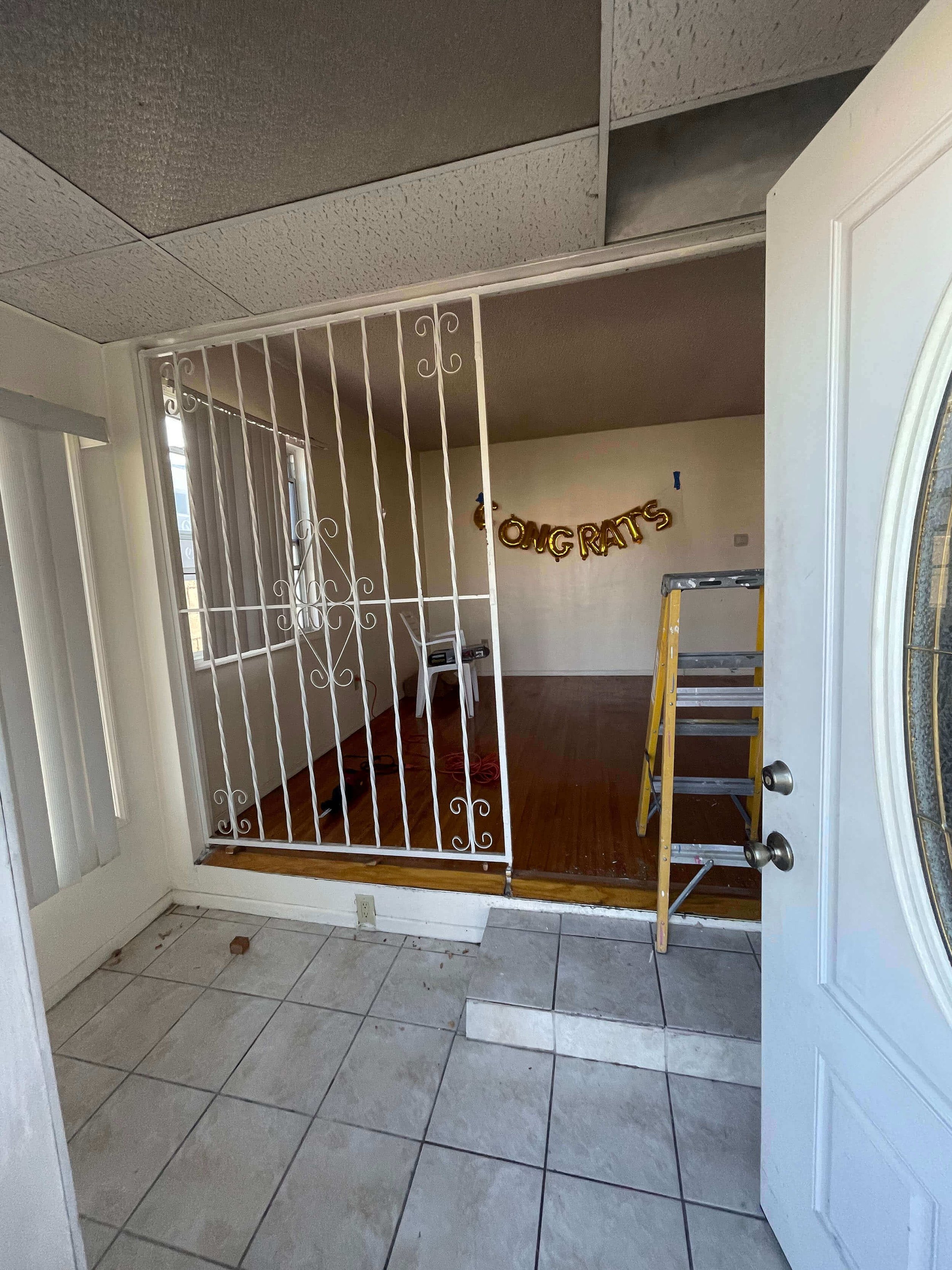 A room at residence 3016 W 83rd St. under renovation with a white decorative metal gate partially blocking the entrance, a yellow step ladder, a wall with an iron gate entrance.