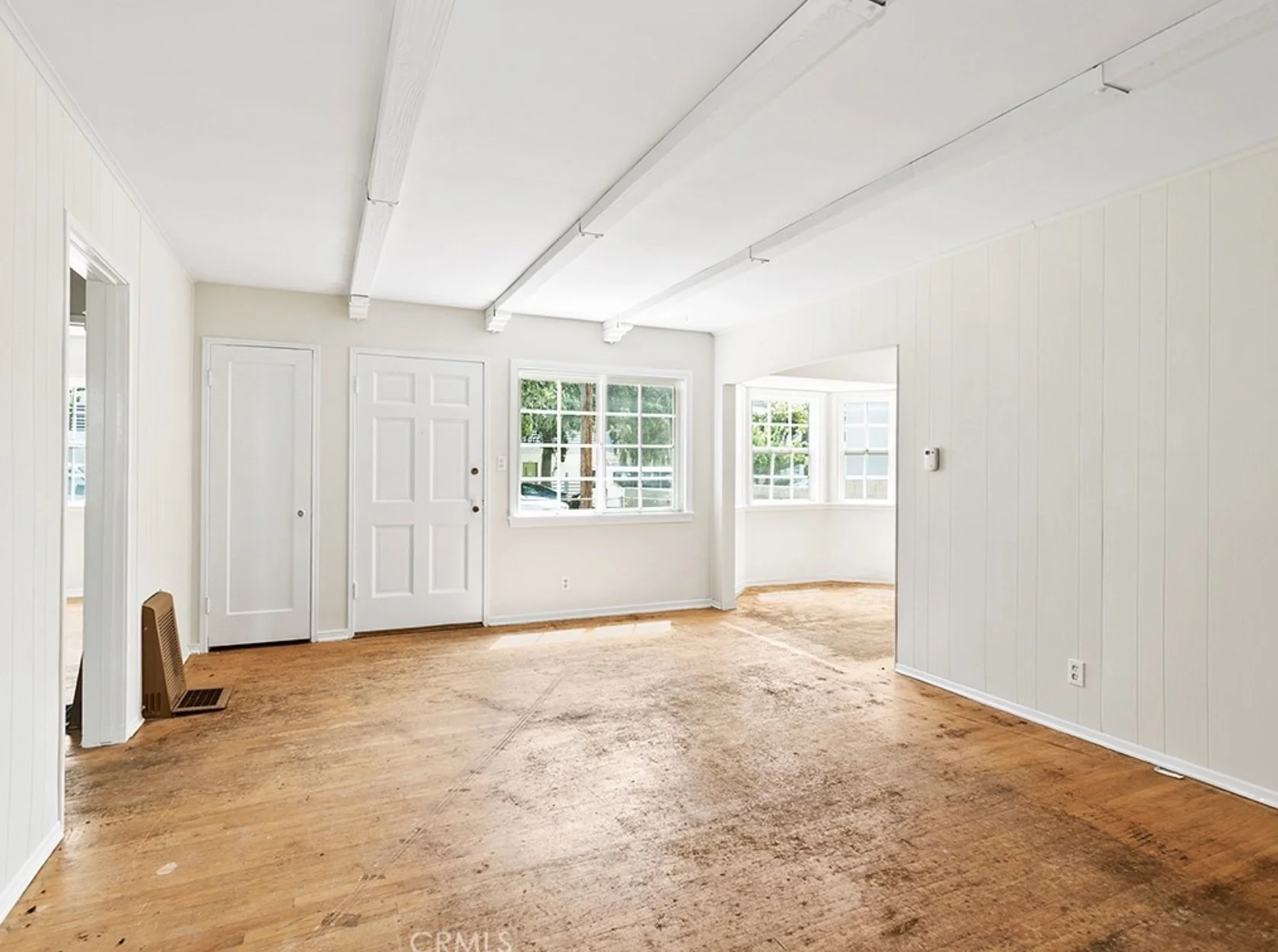 Empty room with white walls, large windows, and a wooden floor, with some visible wear on the flooring at residence 5645 & 5645 ½ Auckland Ave, in North Hollywood, California.