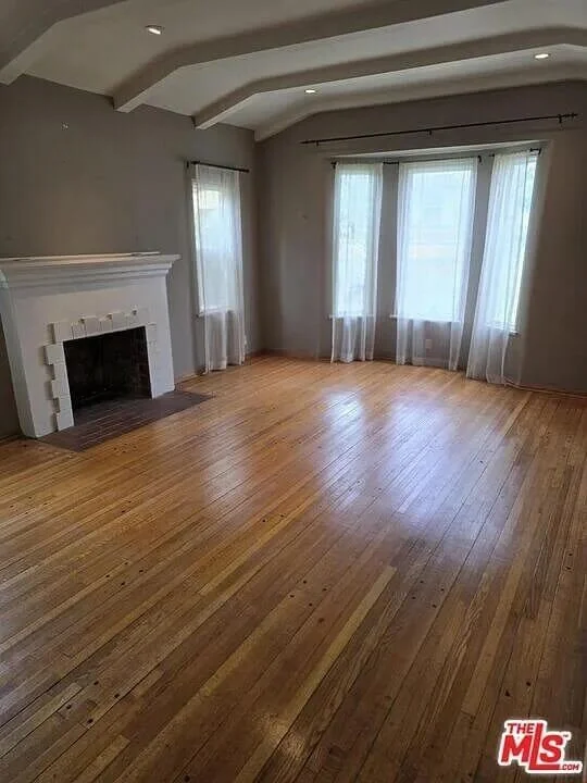 Empty living room with hardwood floors, large windows with white curtains, and a white fireplace at residence 3016 W 83rd St. in Inglewood California.