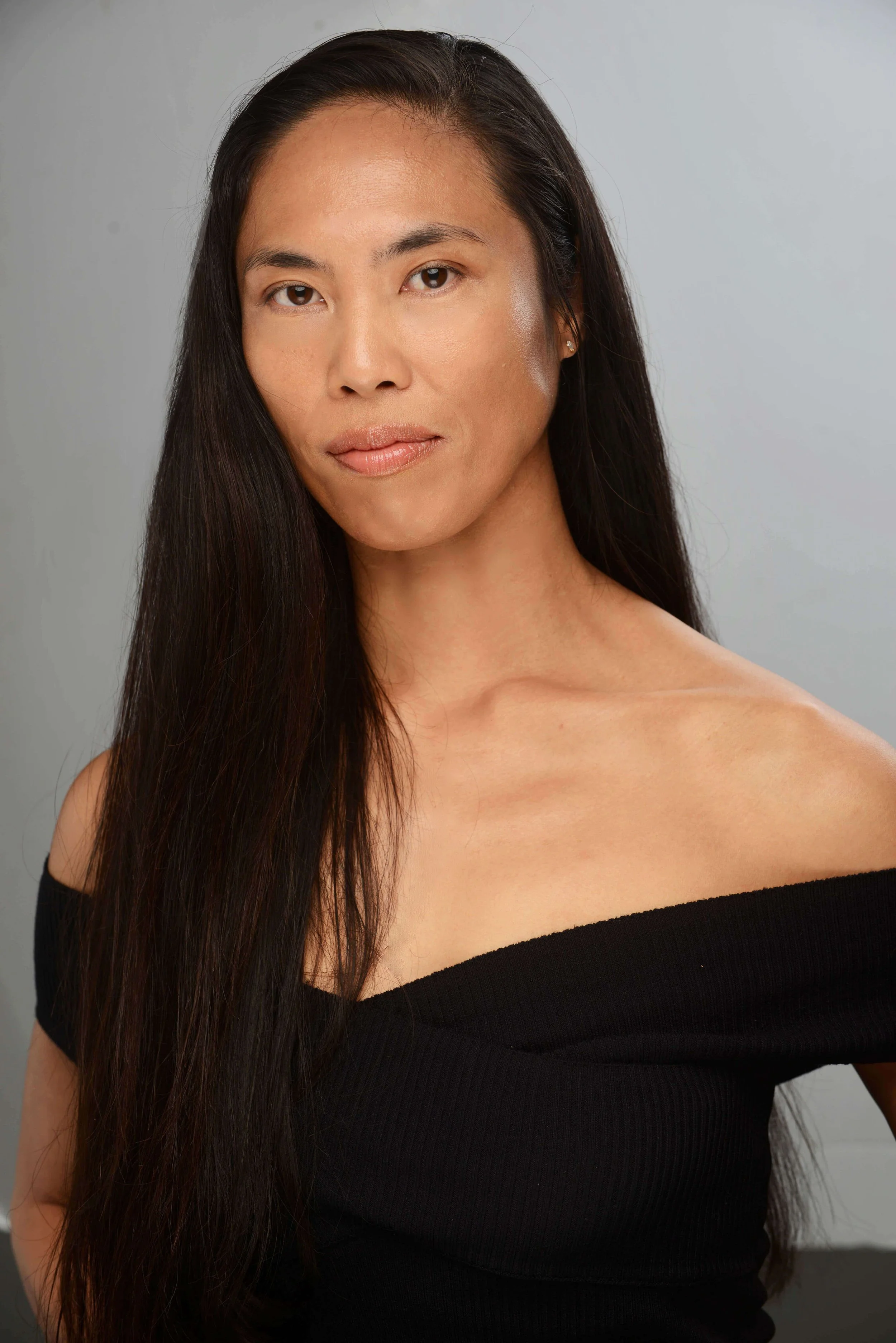 Deborah Yumul: founder of BELLEVRA Group shown in a black dress against a grey background.