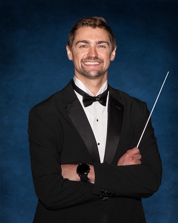A young man with short brown hair, wearing a blue dress shirt and a striped tie, smiling in a professional portrait against a blue background.