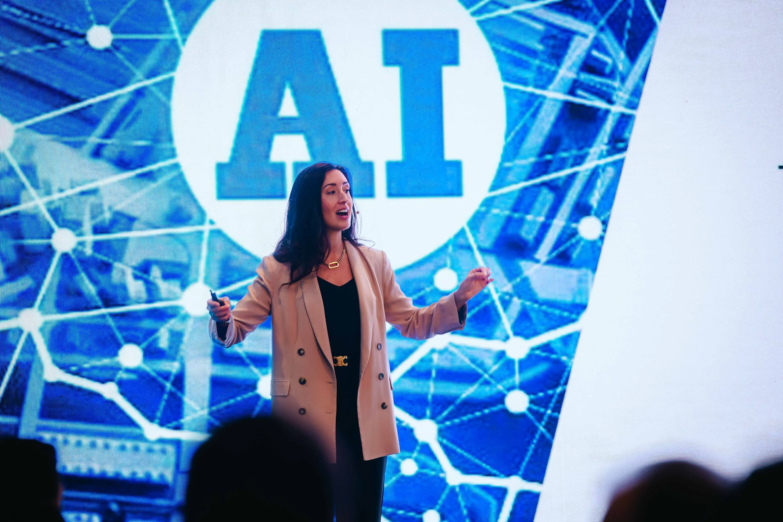 A woman giving a presentation on stage with a background displaying the word 'AI' and a digital network design.