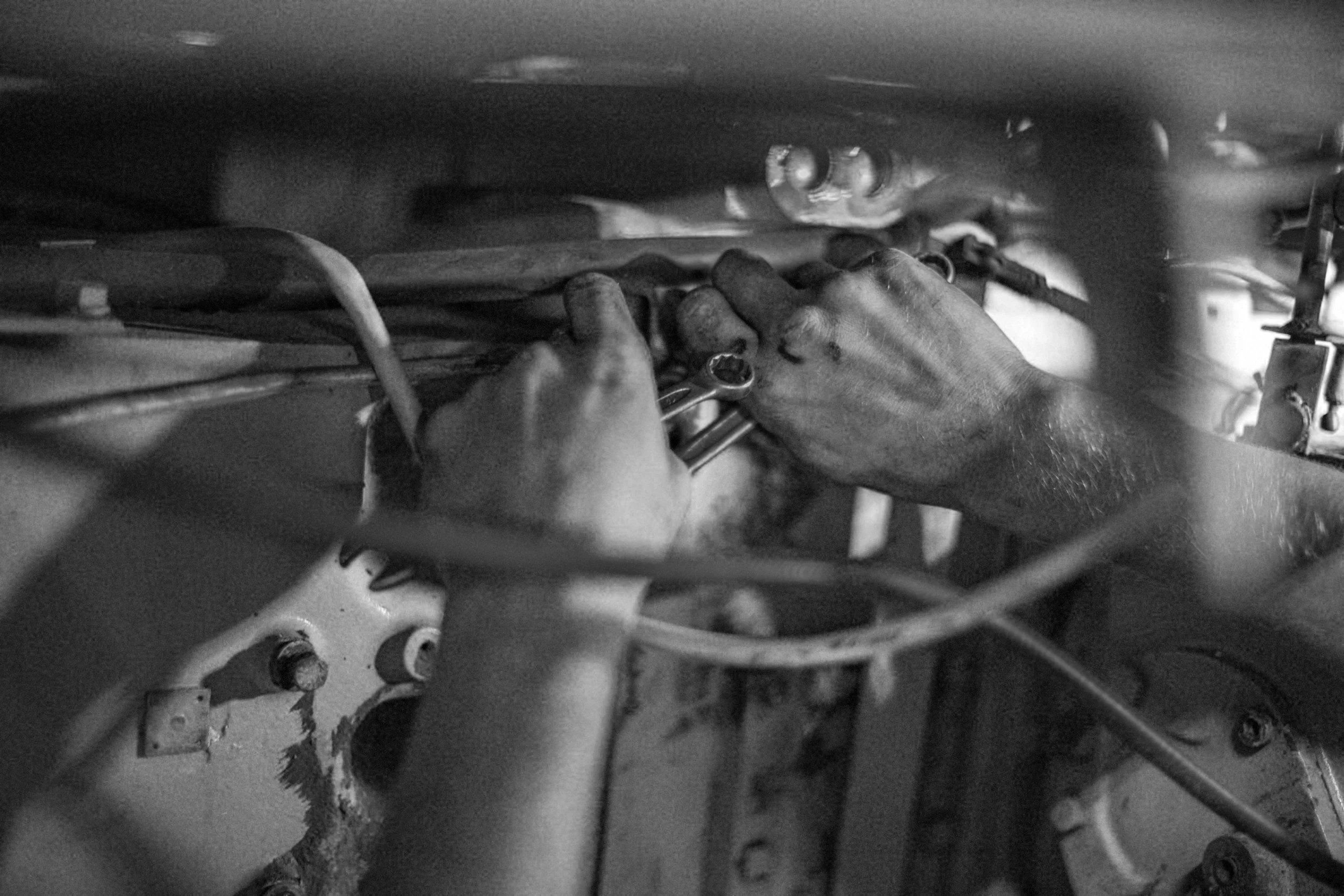 Close-up of a person’s hands working on mechanical components inside a vehicle, using a wrench.