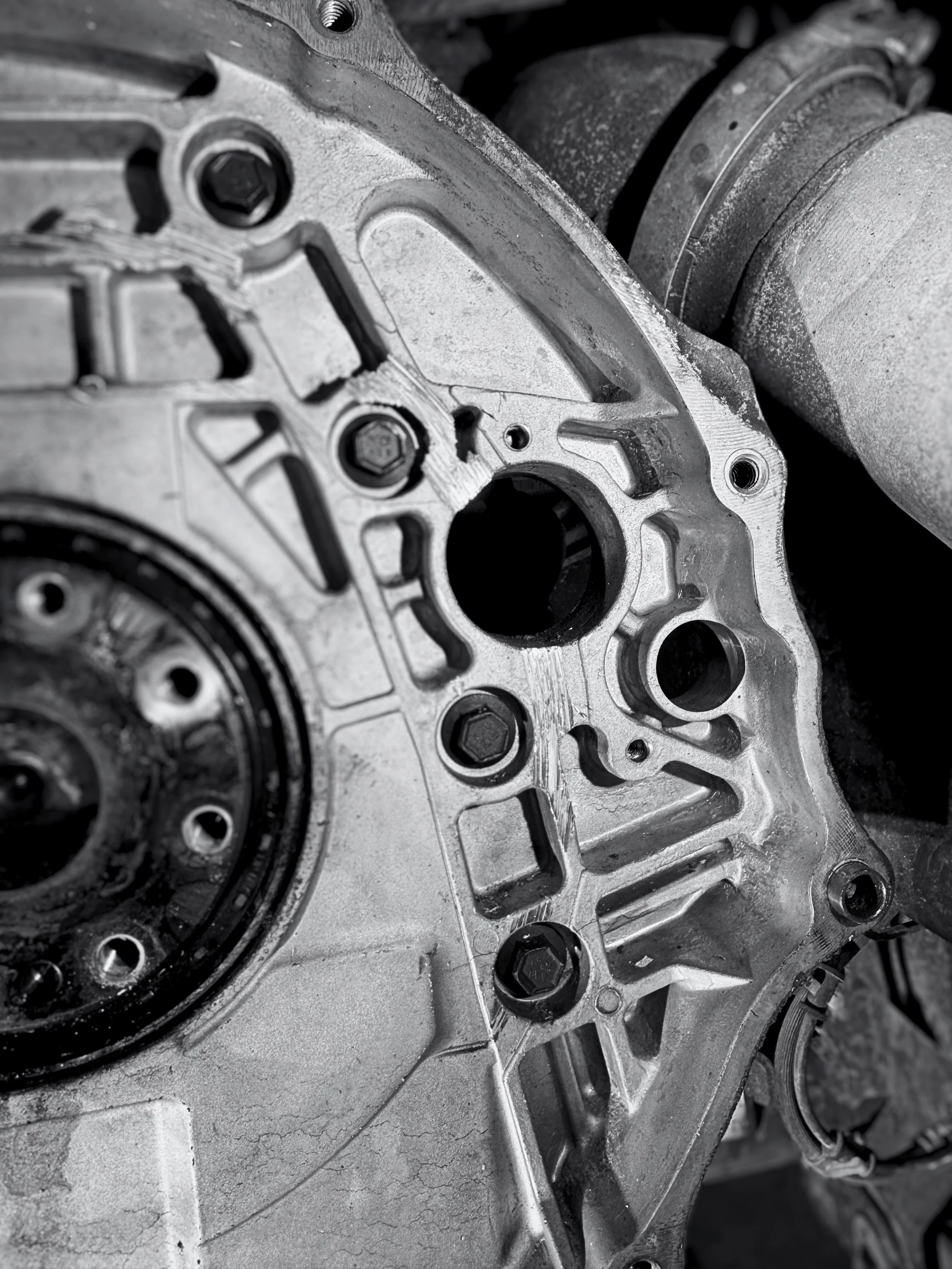 Close-up of a metallic automotive engine component with bolt holes and intricate machined details in black and white.