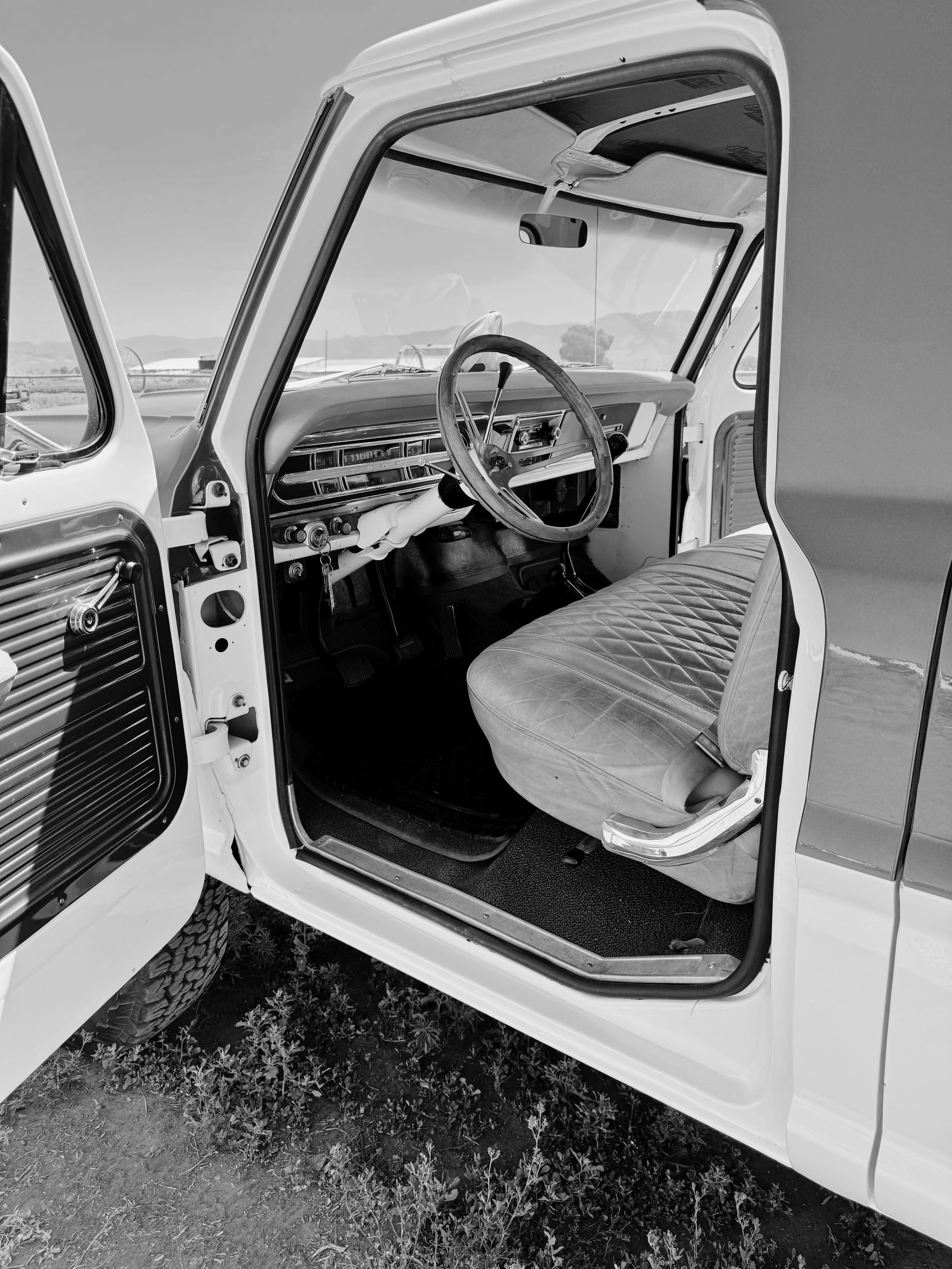Interior of a vintage truck with a bench seat, steering wheel, and dashboard.