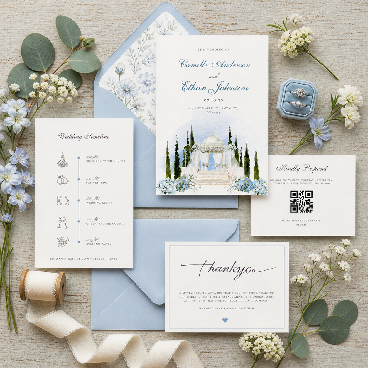 Elegant wedding invitation suite flat lay featuring soft blue envelopes with coordinating floral liners, a central invitation with a watercolor gazebo illustration, matching RSVP and timeline cards, and a thank you card, styled with neutral ribbon, g