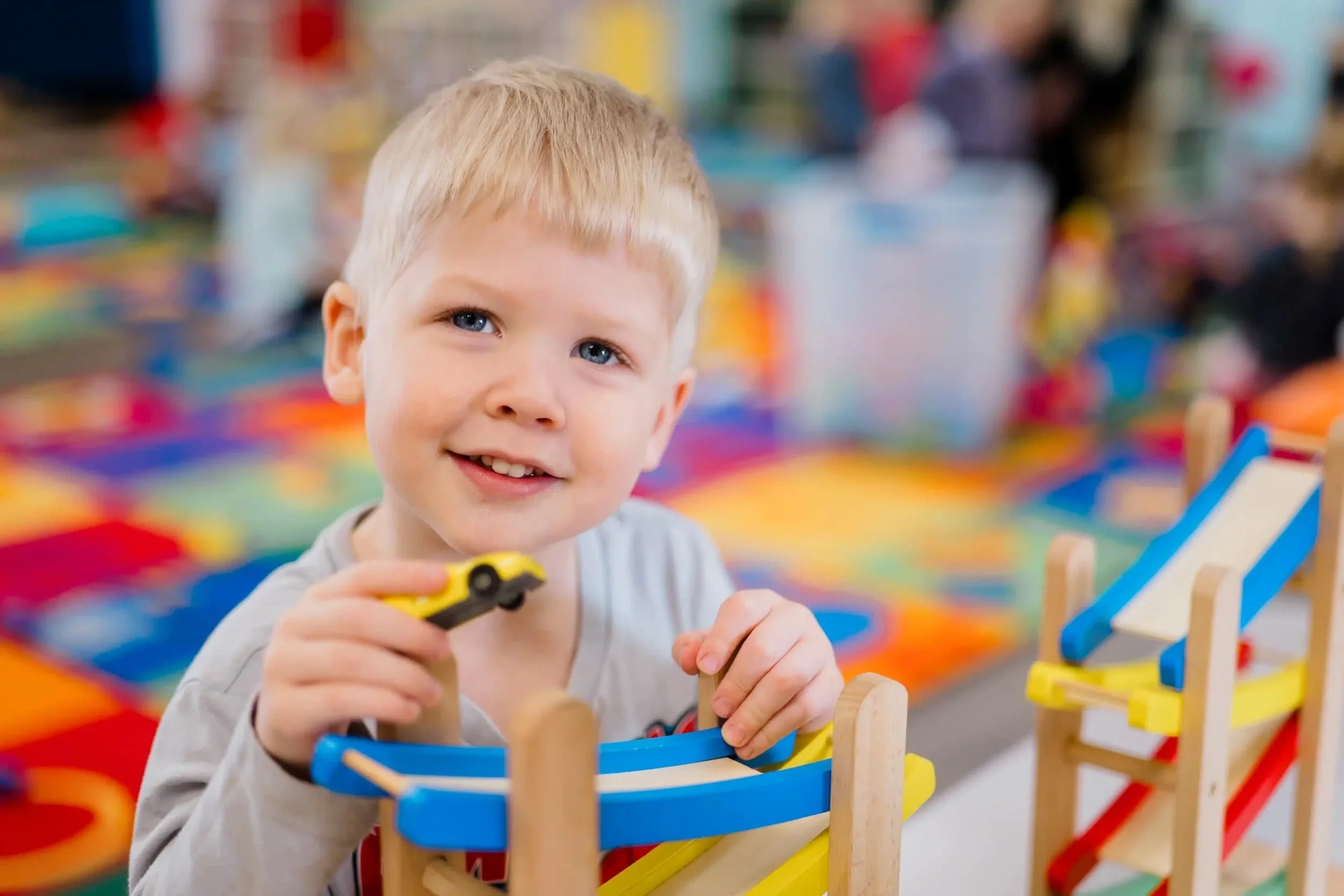 kid smiling at the camera and holding a yellow toy car.