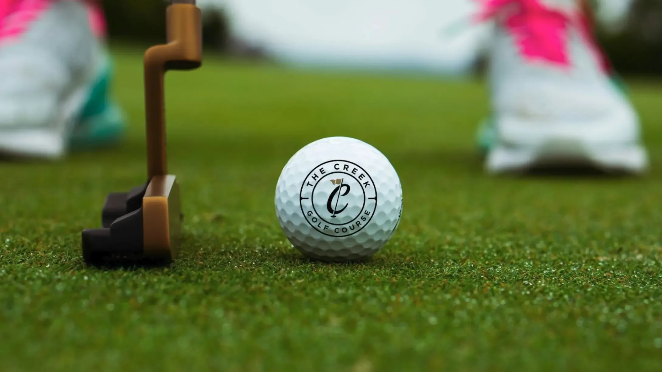 A branded golf ball on a green course showing The Creek Golf Course logo