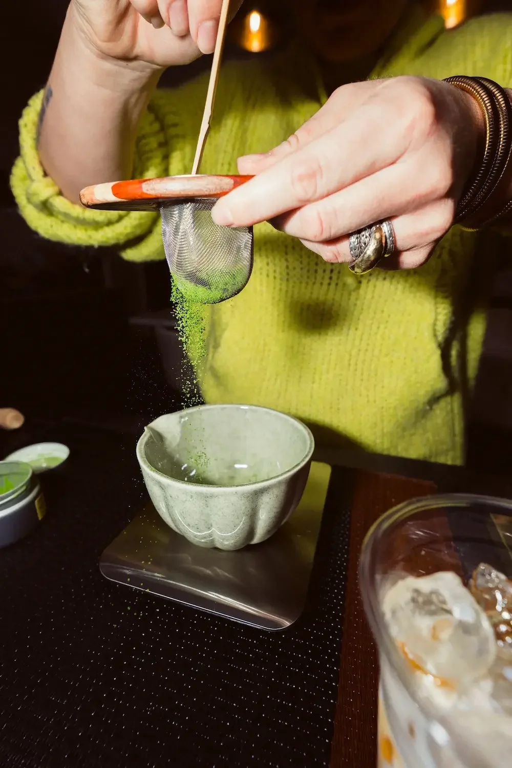 Up close photo of a woman sifting Matcha powder on top of a iced matcha drink
