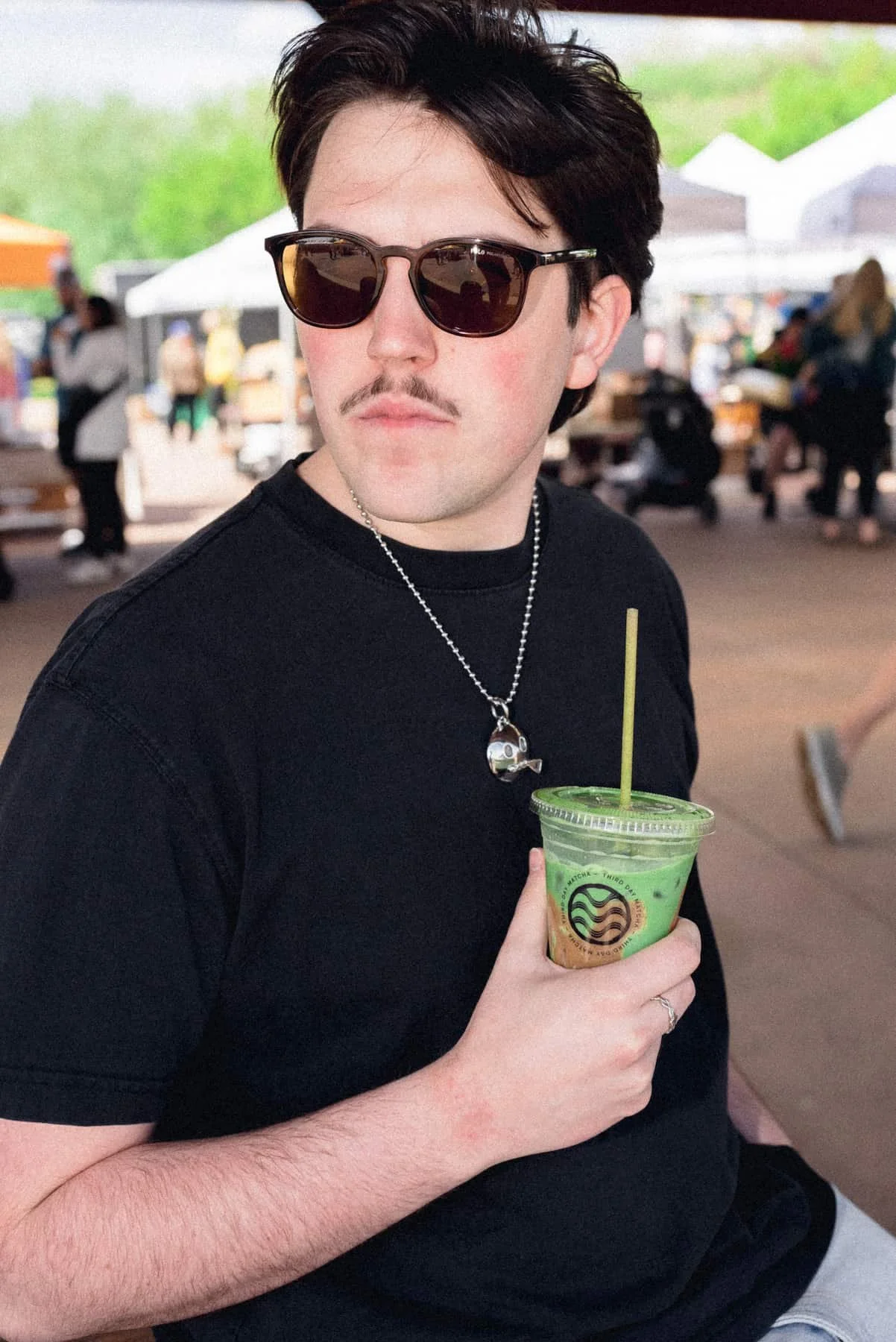 Man in sunglasses looking off and holding matcha.