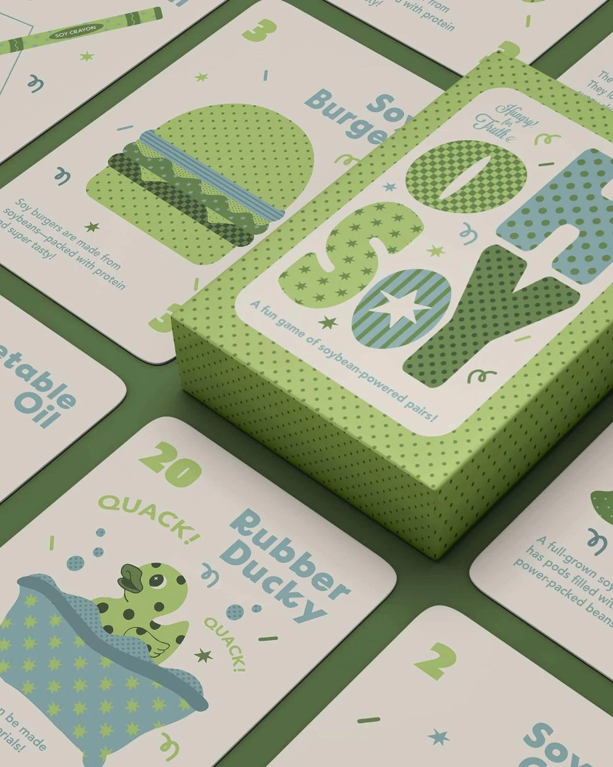 Set of cards and a box for a soybean-powered educational game featuring illustrations of a soybean burger, a rubber duck, and various game instructions in green, blue, and white colors.