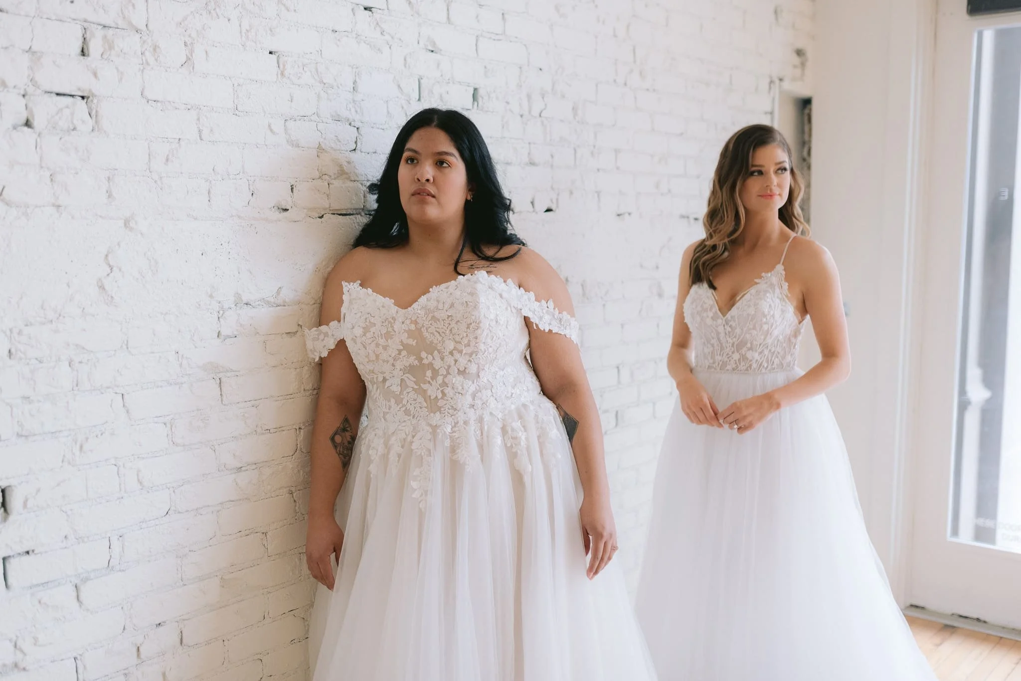 Two models in wedding dresses posing inside Marie & Marie Bridal.
